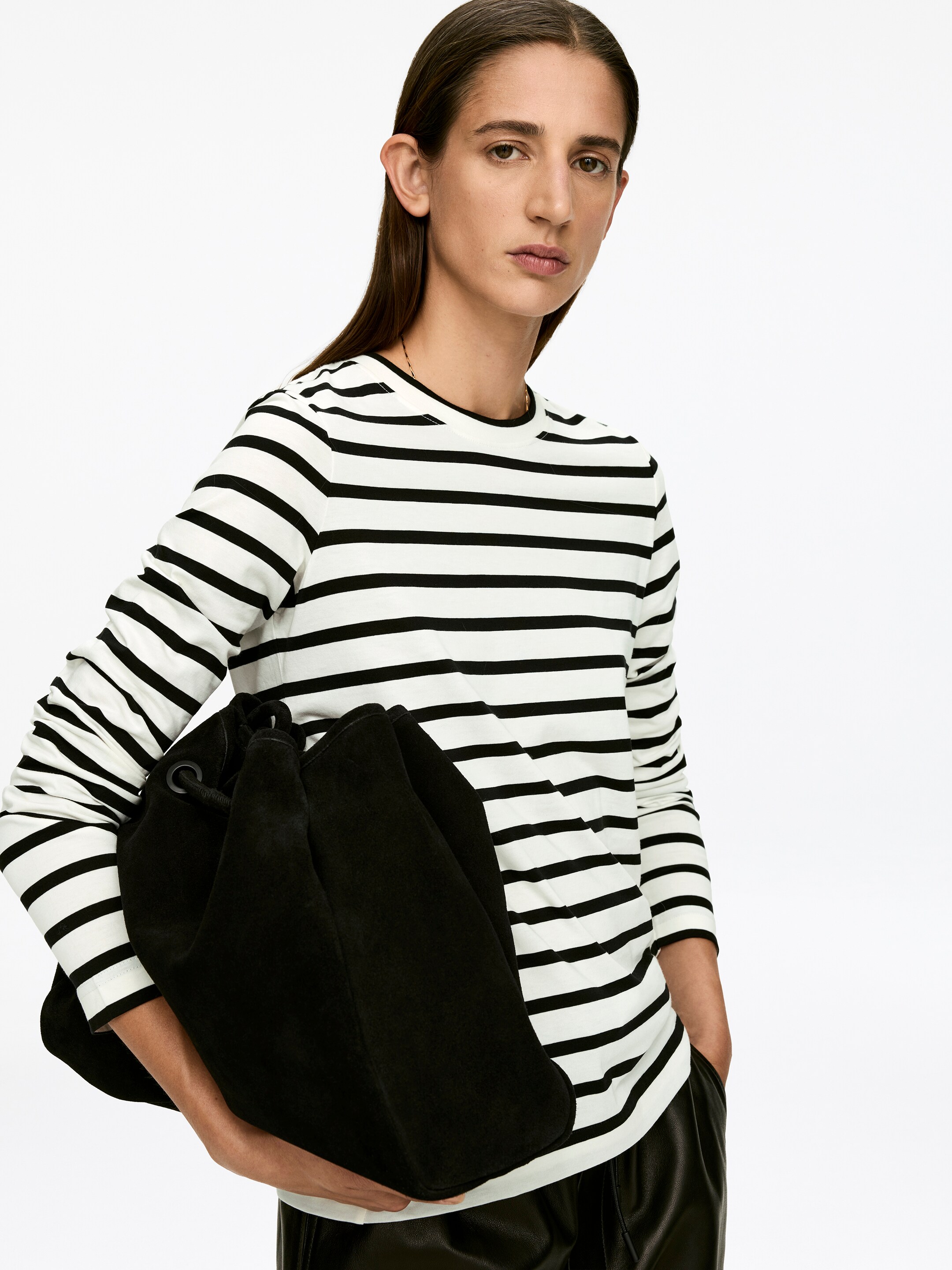 Se større billede: En T-shirt med sorte og hvide vandrette striber, lange ærmer uden manchetter og en ribbet rund hals bæres af modellen. Modellen holder en sort snørepose mod forsiden af T-shirten.