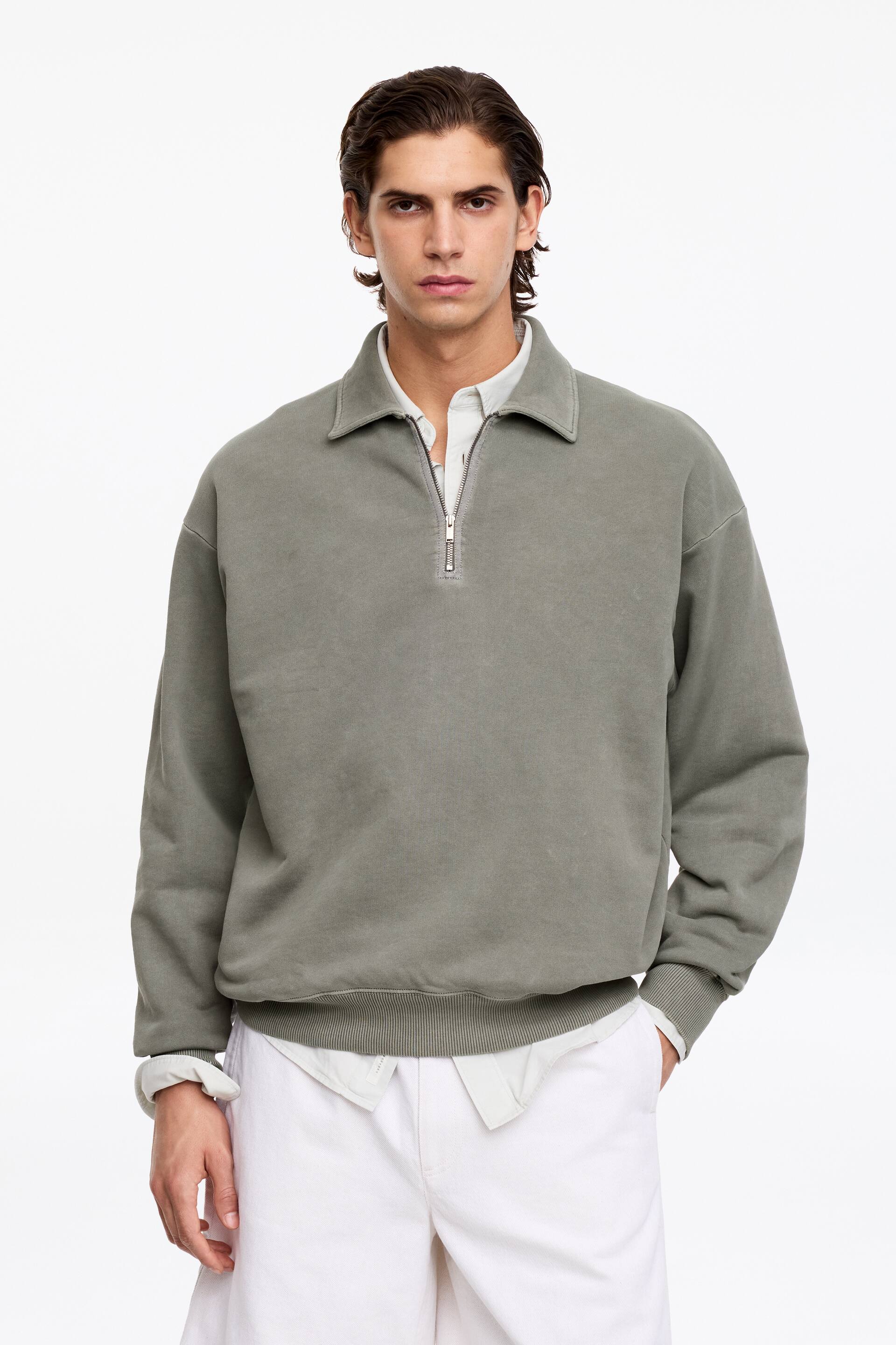View larger image: A faded grey quarter-zip sweatshirt featuring a spread collar and a silver-toned zip extending to the chest. It showcases ribbed cuffs and a ribbed hem, with an off-white shirt layered underneath, peeking out at the collar and hem.