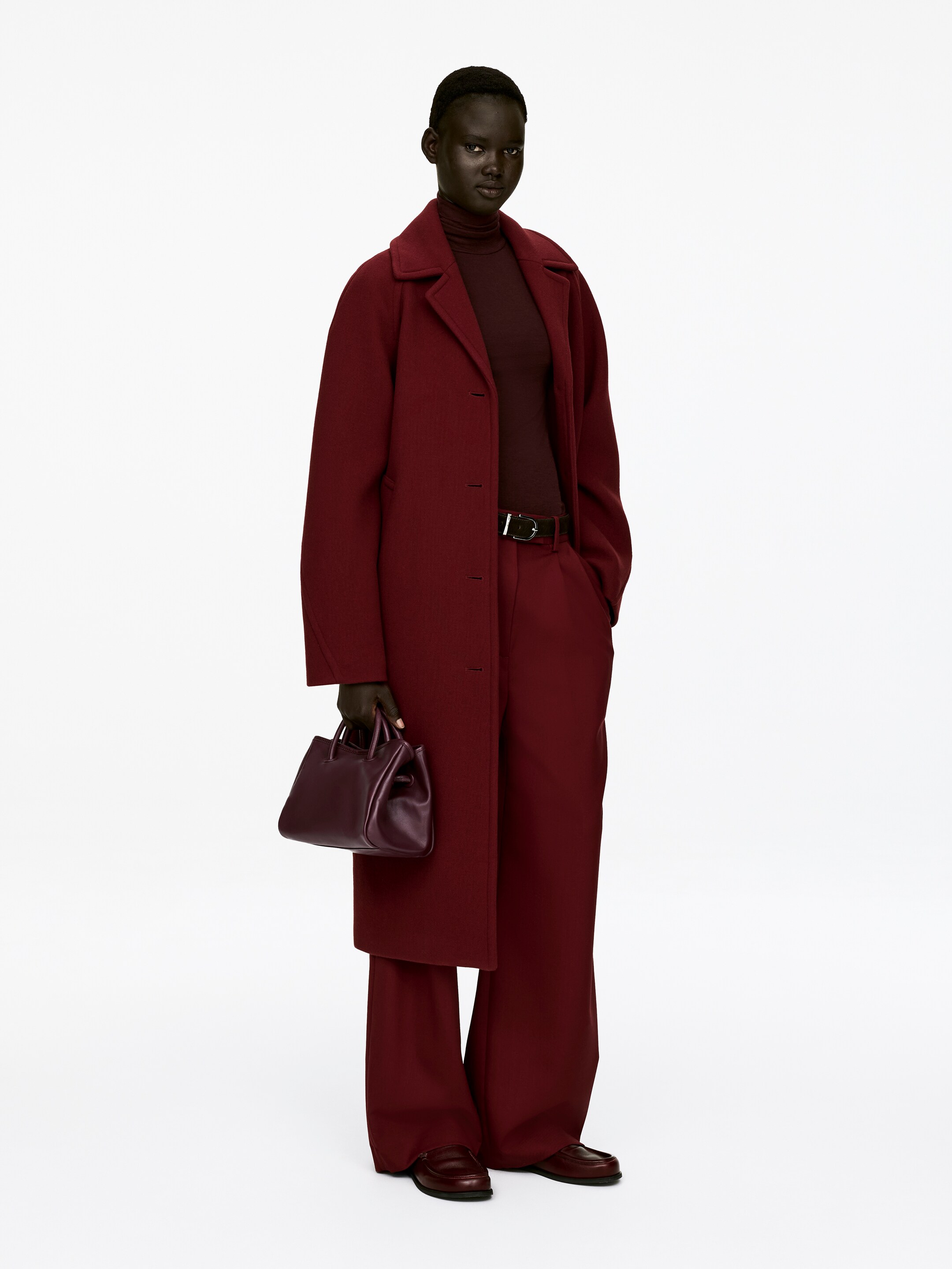 Visualizza immagine più grande: Una borsa a tracolla in pelle rosso scuro, con manici superiori strutturati, è tenuta dalla modella.