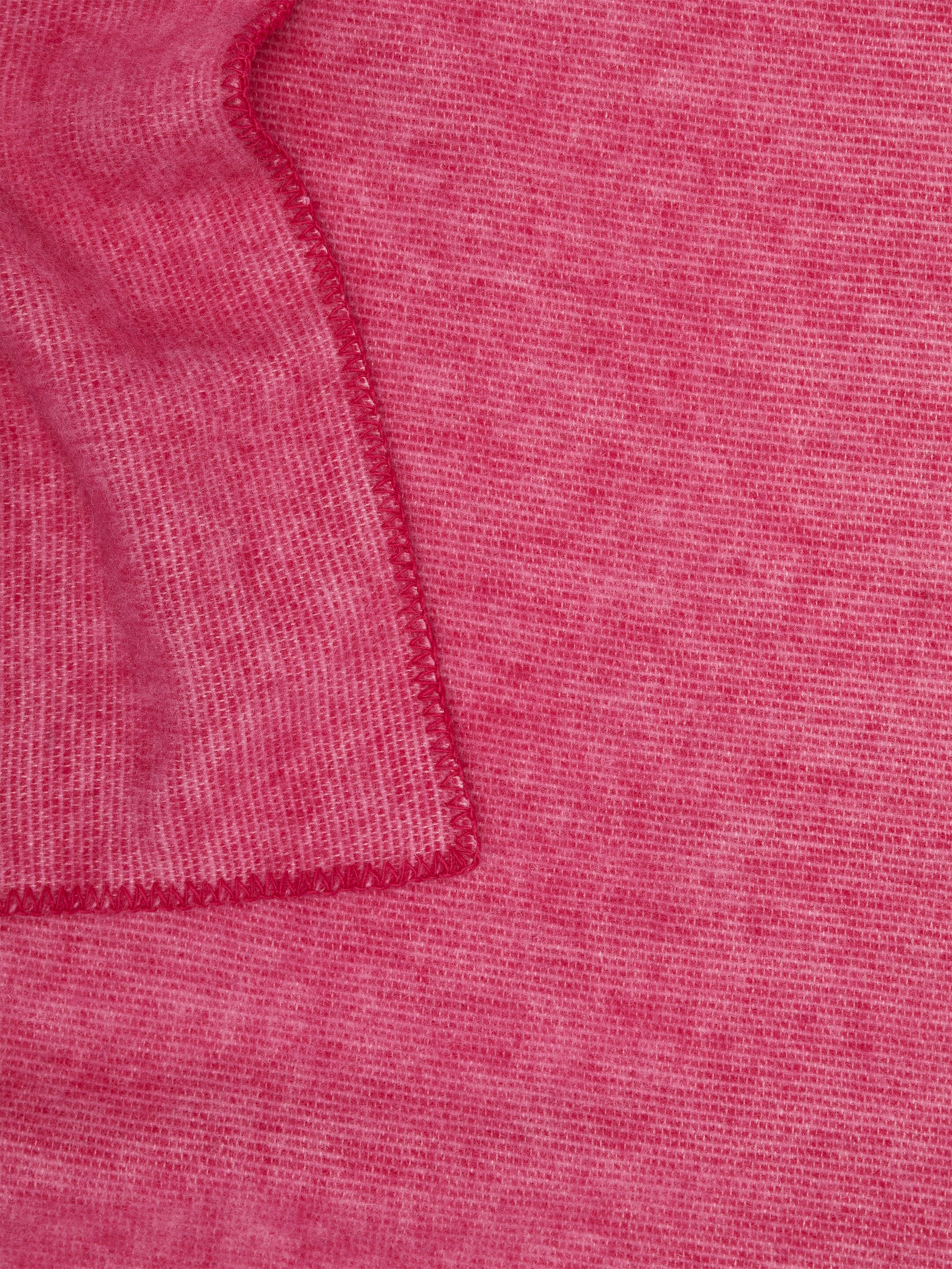 View larger image: A solid pink blanket is displaying a visible, slightly textured weave, with prominent blanket stitching finishing its edges. It is folded, showing one section layered over another.