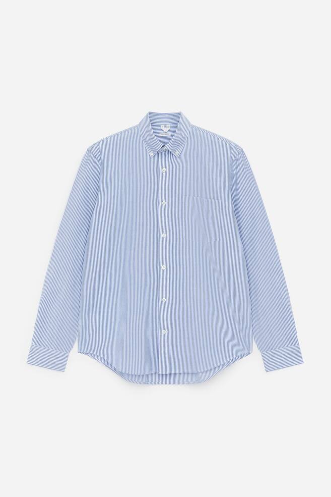 A front view of an Oxford shirt is displaying blue and white vertical stripes. It is presenting a button-down collar, a full-length front button placket with white buttons, a single patch pocket on the left chest, long sleeves with single-button barrel cuffs, and a curved hem. - 1