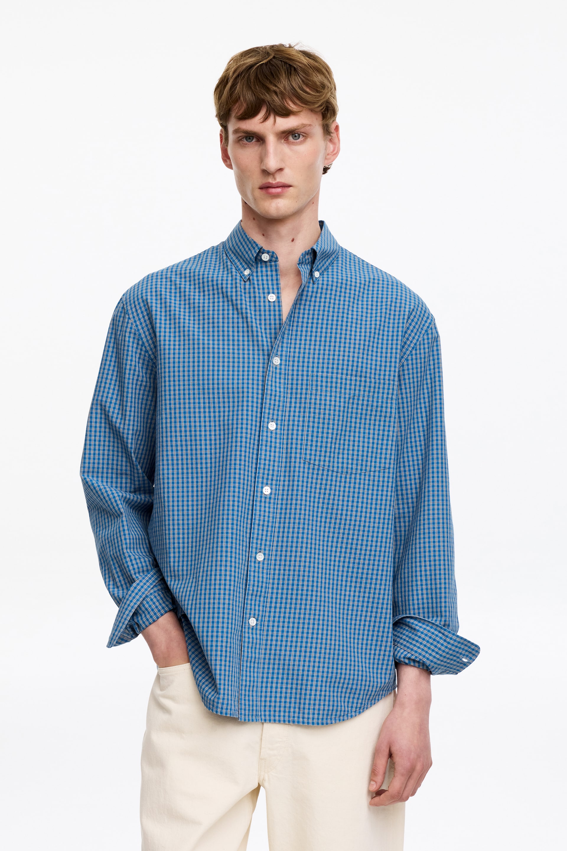 Grotere afbeelding bekijken: Een blauw-wit geruite overhemd wordt frontaal gepresenteerd, met een button-down kraag en witte knopen langs de voorbies. De lange mouwen zijn opgerold bij de manchetten en het overhemd heeft een ontspannen pasvorm.