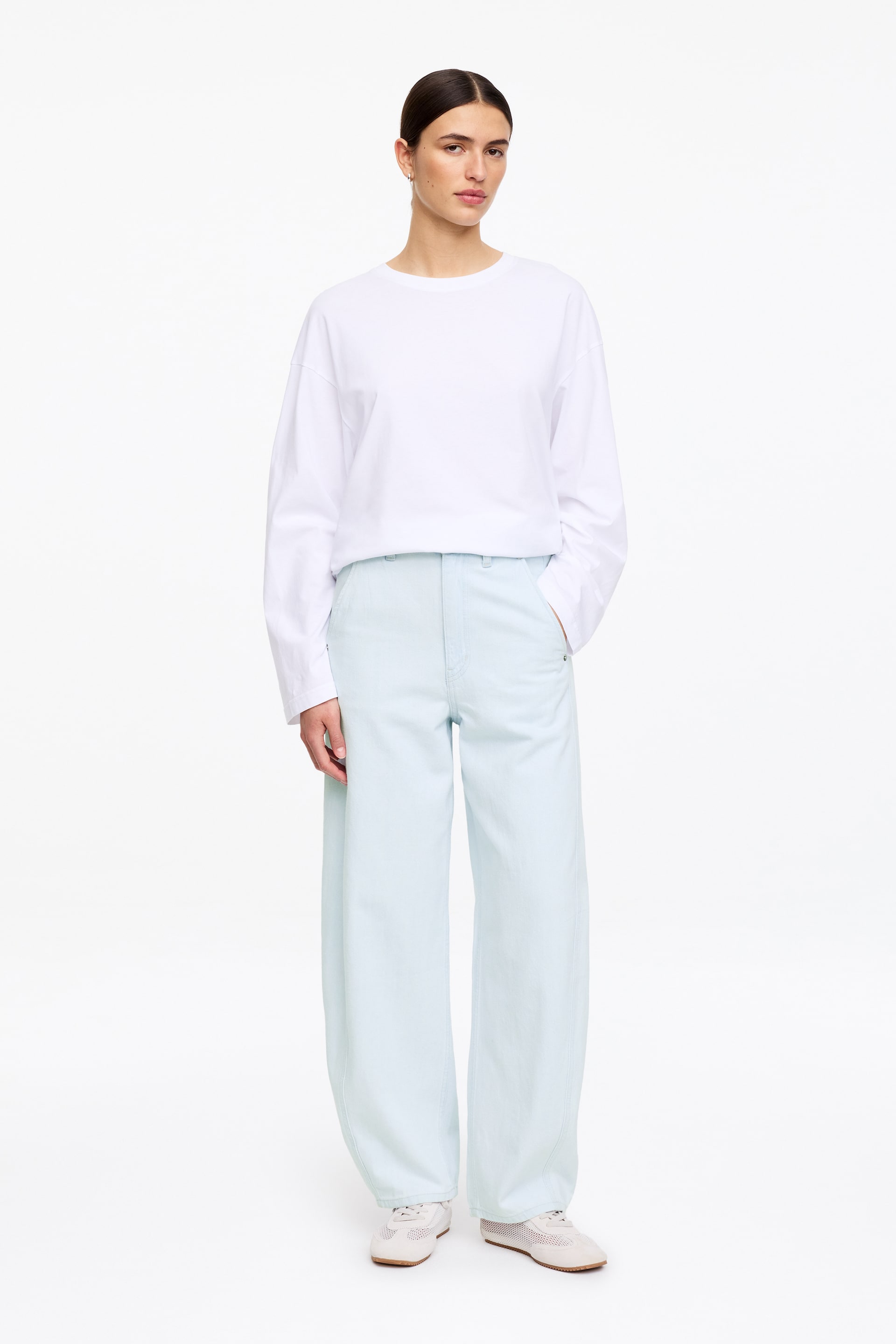 Se større billede: En hvid langærmet top med rund hals og sænkede skuldre bæres nede i lyseblå, højtaljede bukser med brede ben og er parret med hvide sneakers, alt præsenteret fra en frontvendt vinkel.
