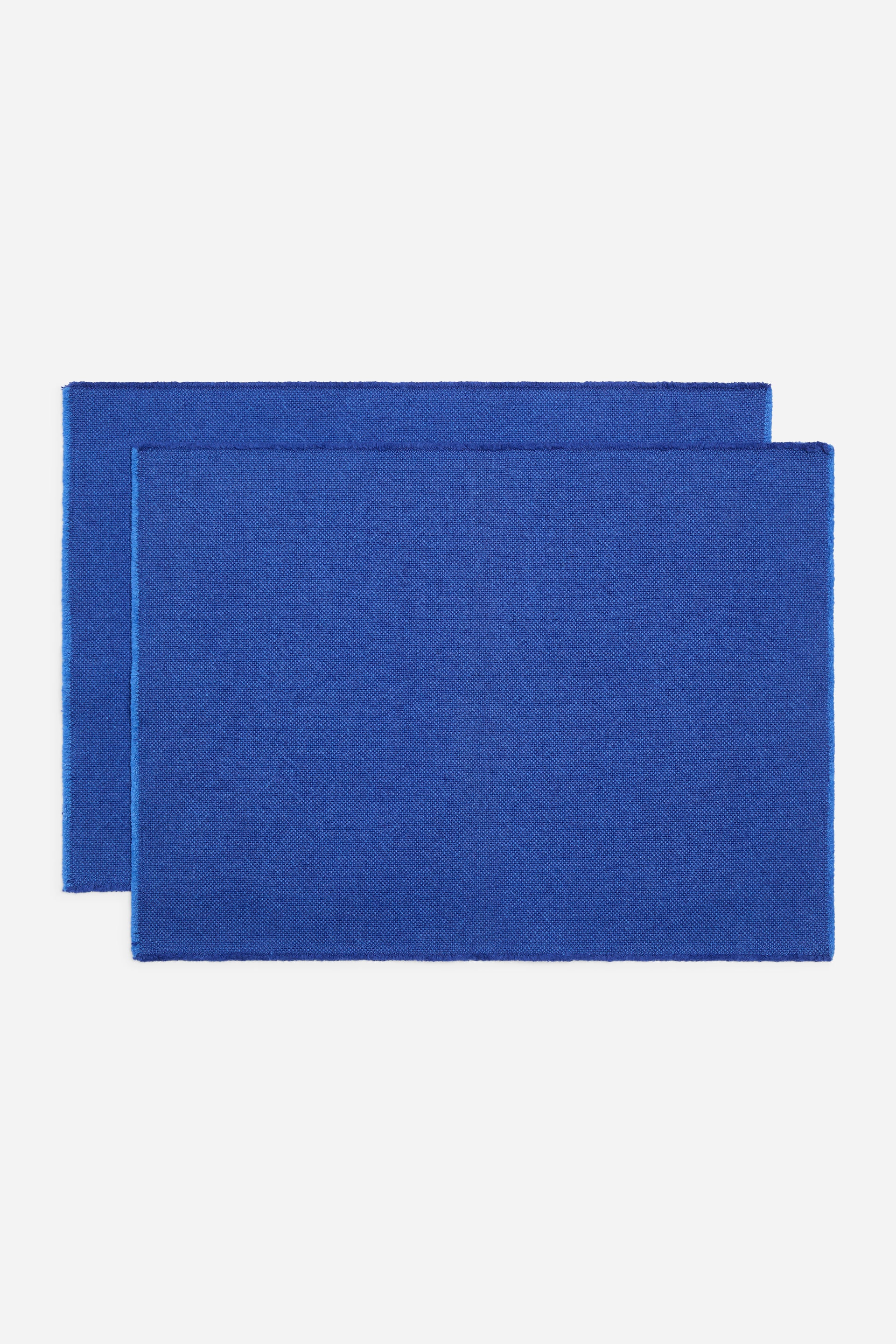 View larger image: Two rectangular placemats display a vibrant blue colour and a visible woven texture. They feature slightly softened edges, with one placemat positioned slightly behind the other.