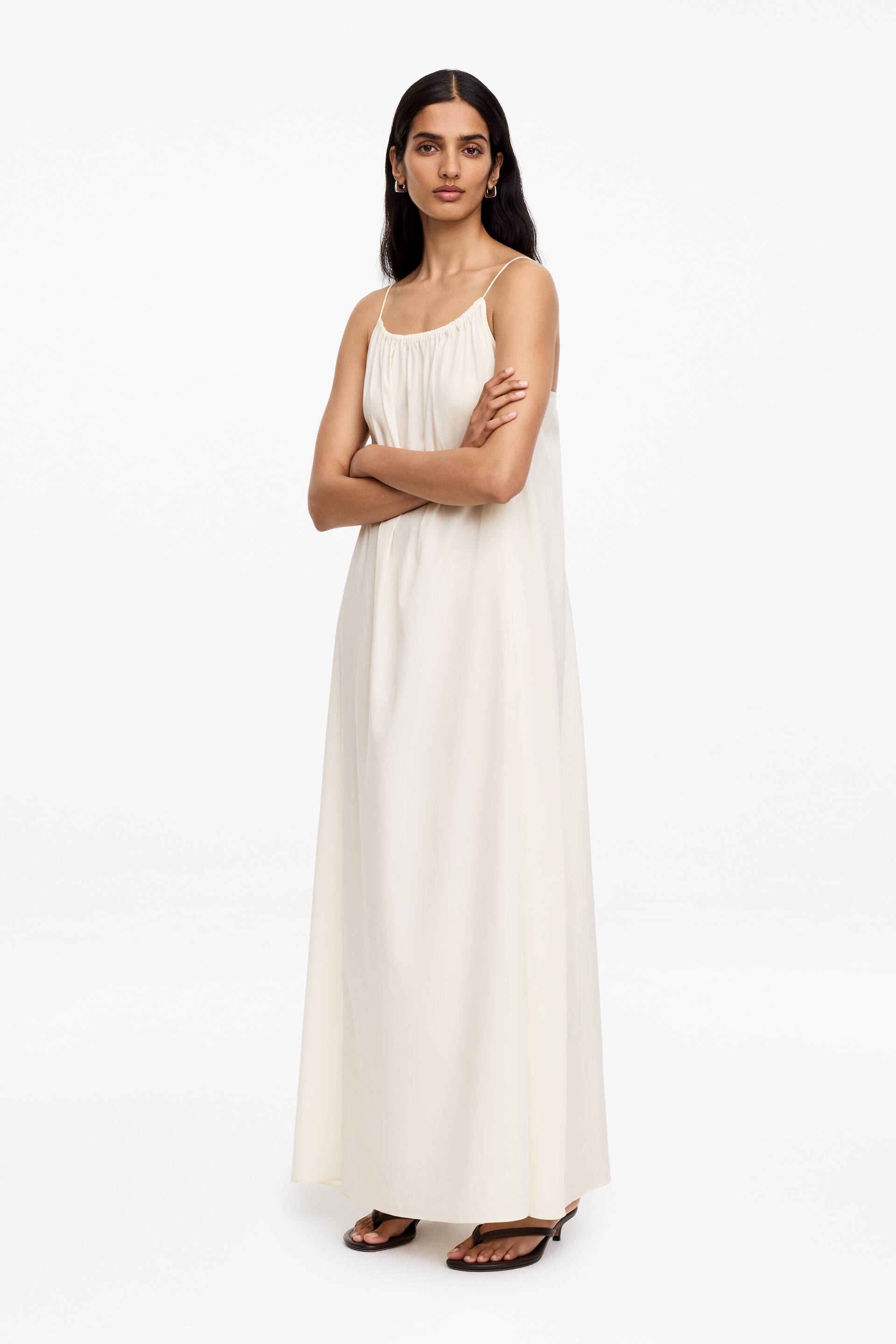 Grotere afbeelding bekijken: De off-white maxi-jurk heeft dunne spaghettibandjes en een geplooide halslijn, en valt losjes naar de vloer in een A-lijn silhouet.