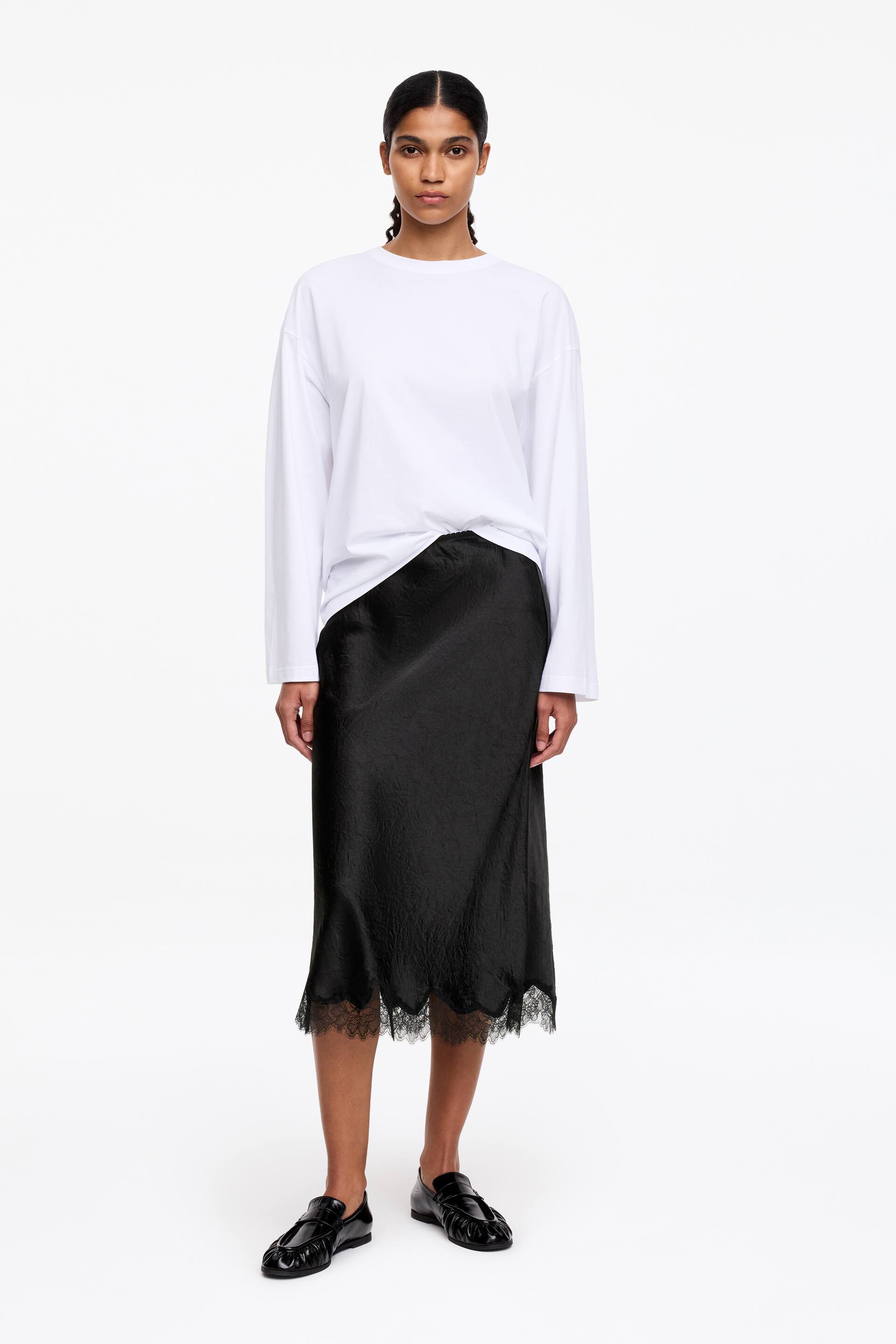 Преглед на по-голямо изображение: Черна миди пола, която се спуска с фина намачкана текстура. Нейният вълнообразен подгъв е изкусно украсен с черна дантела.