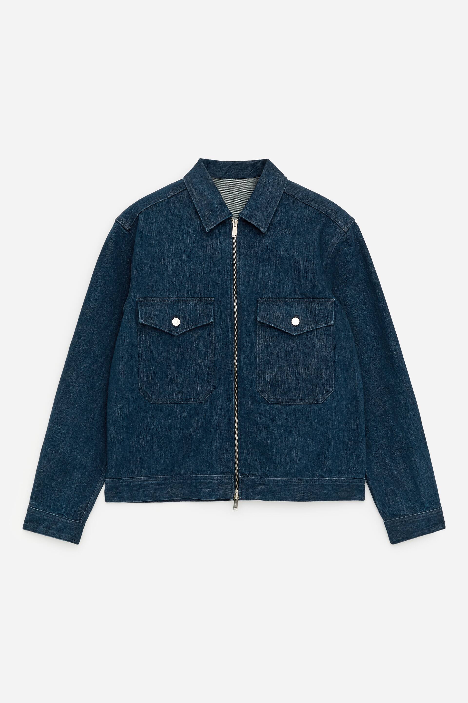 Visualizza immagine più grande: Una giacca di jeans blu scuro mostra la sua PARTE ANTERIORE, caratterizzata da una chiusura a cerniera argentata a tutta lunghezza. Due tasche applicate con patte e chiusure a scatto argentate sono visibili sul petto, ed è progettata con un colletto a punta e maniche lunghe.