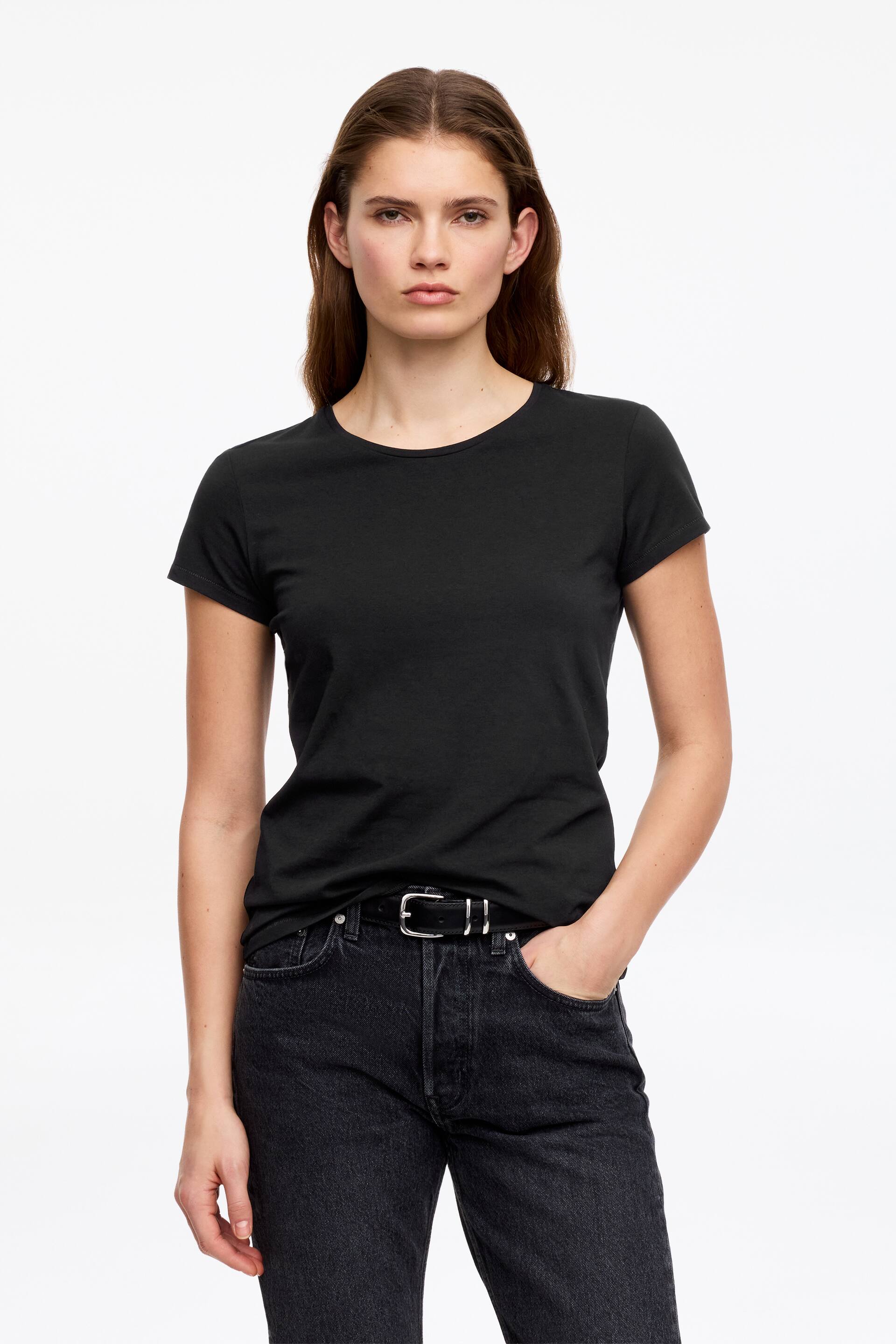 Visa större bild: En svart figursydd t-shirt med rund hals och korta ärmar. Den presenteras framifrån och är instoppad i mörktvättade jeans.