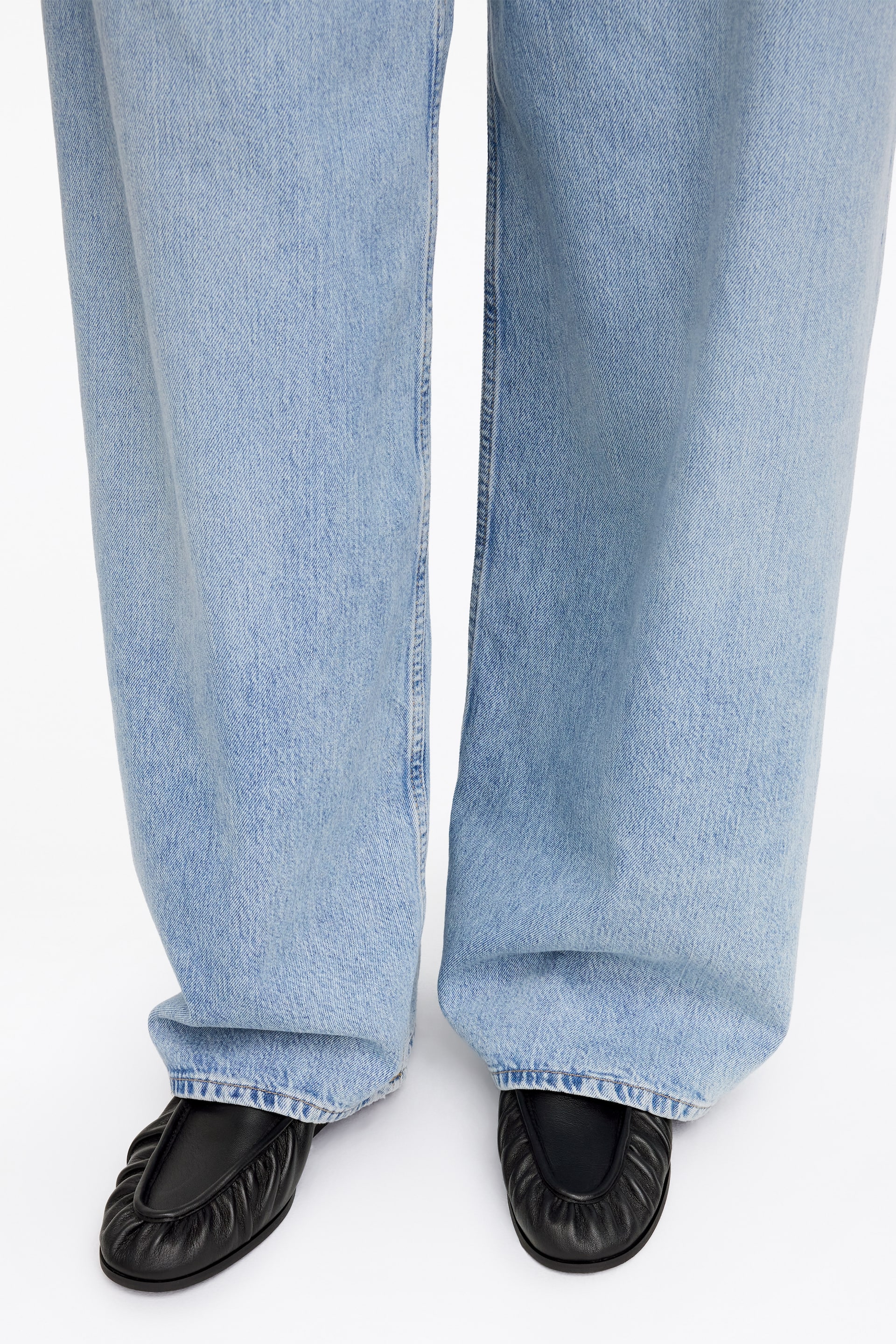 Agrandir l'image: Chaussures plates en cuir noir avec un dessus plissé et un bout arrondi, associées à un jean large bleu clair tombant sur le dessus.