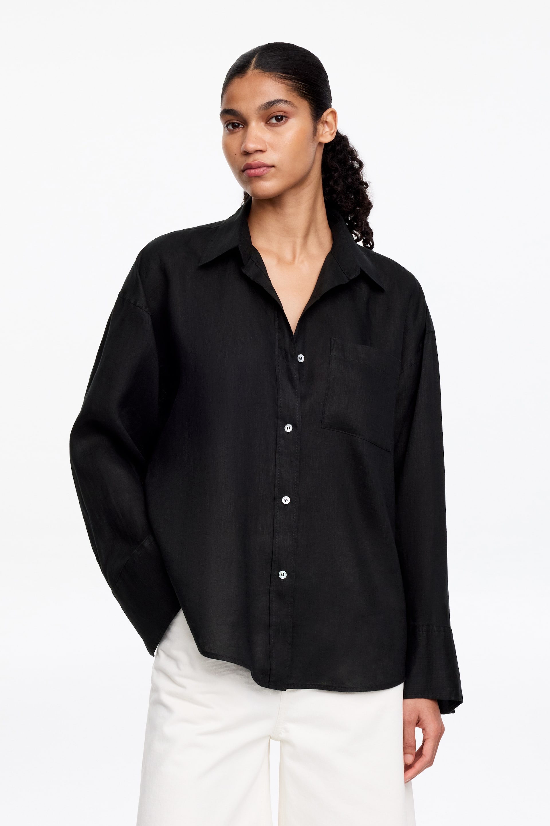 Ver imagen más grande: Una camisa negra texturizada presenta un cuello extendido, una tapeta completa de botones con botones blancos y un bolsillo de parche en el pecho izquierdo. Se presenta con un ajuste oversize, mangas largas y relajadas, y puños anchos, orientados hacia adelante.