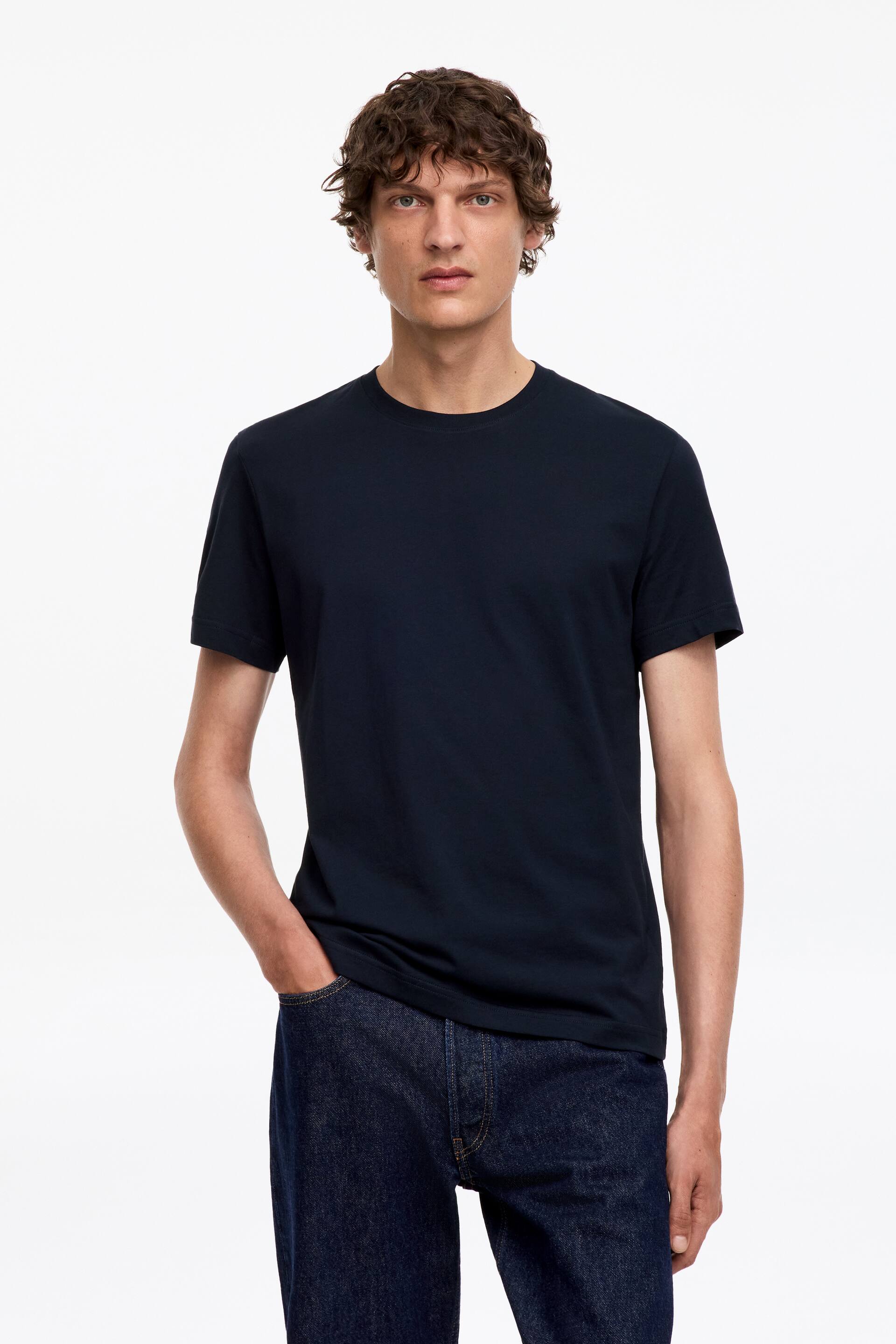 Visualizza l'immagine ingrandita: La modella indossa una T-shirt girocollo blu scuro con una vestibilità su misura e maniche corte. La modella è in piedi, abbinando la T-shirt a jeans scuri.