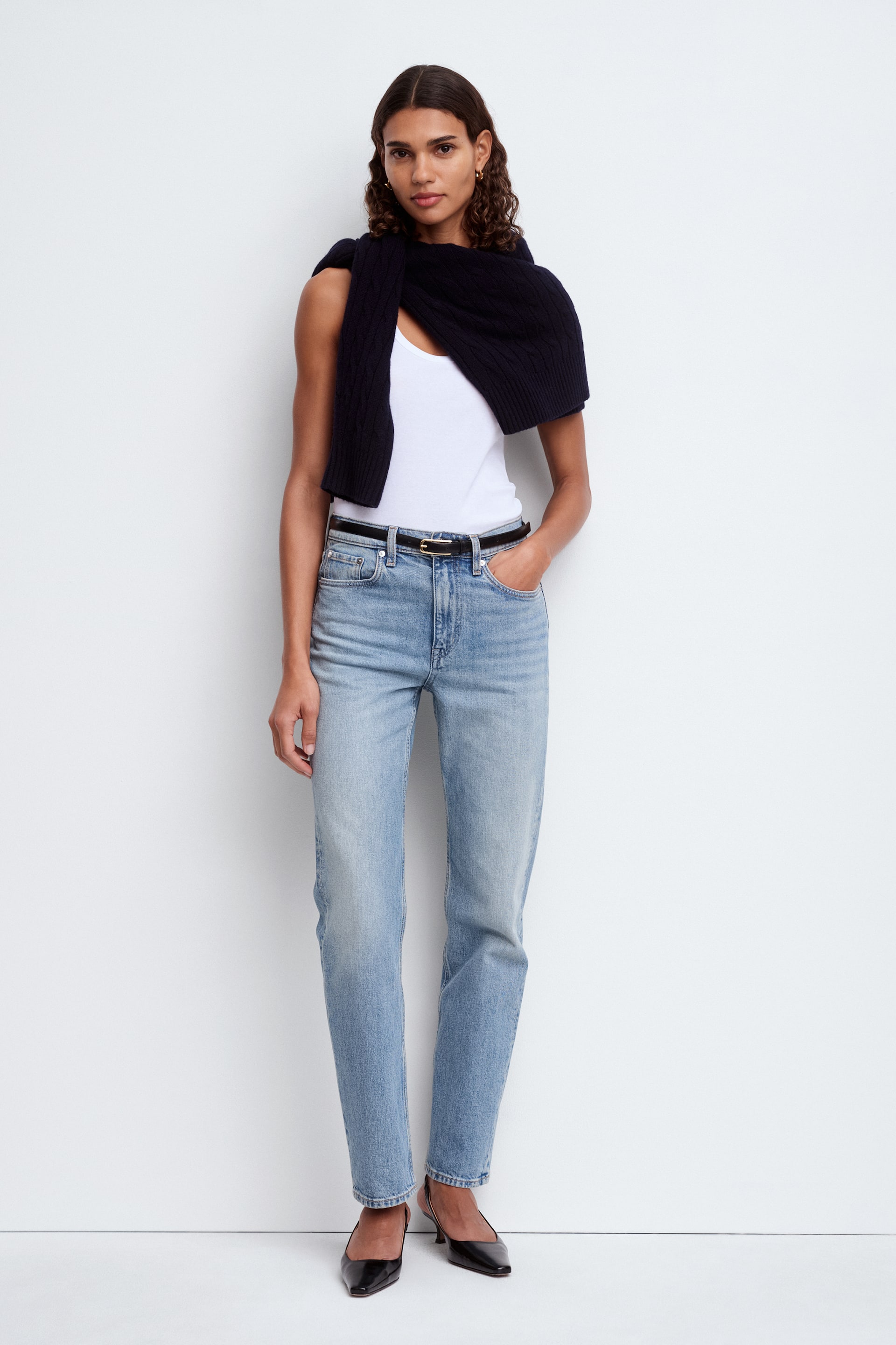 Se større billede: Lyseblå vaskede jeans præsenteres, med et lige ben og et højtaljet design. De fremviser diskret falmning og whiskering på lårene, med et sort bælte trukket gennem bæltestropperne og sømmen hvilende lige over anklerne.
