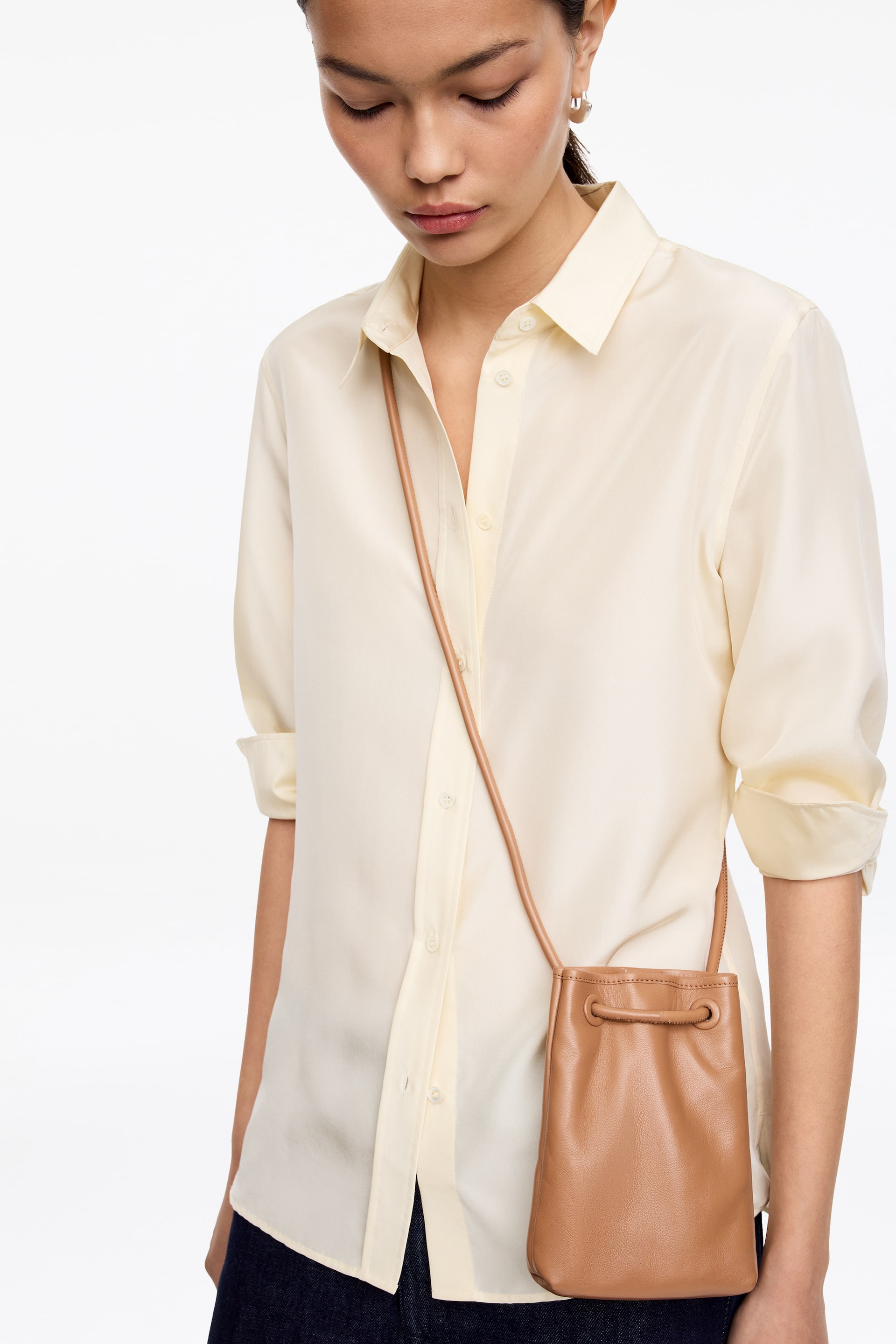 View larger image: A small tan pouch bag is hanging on the wearer's right side, facing forward. It features a soft texture, a drawstring closure cinching its top, and a thin matching strap.