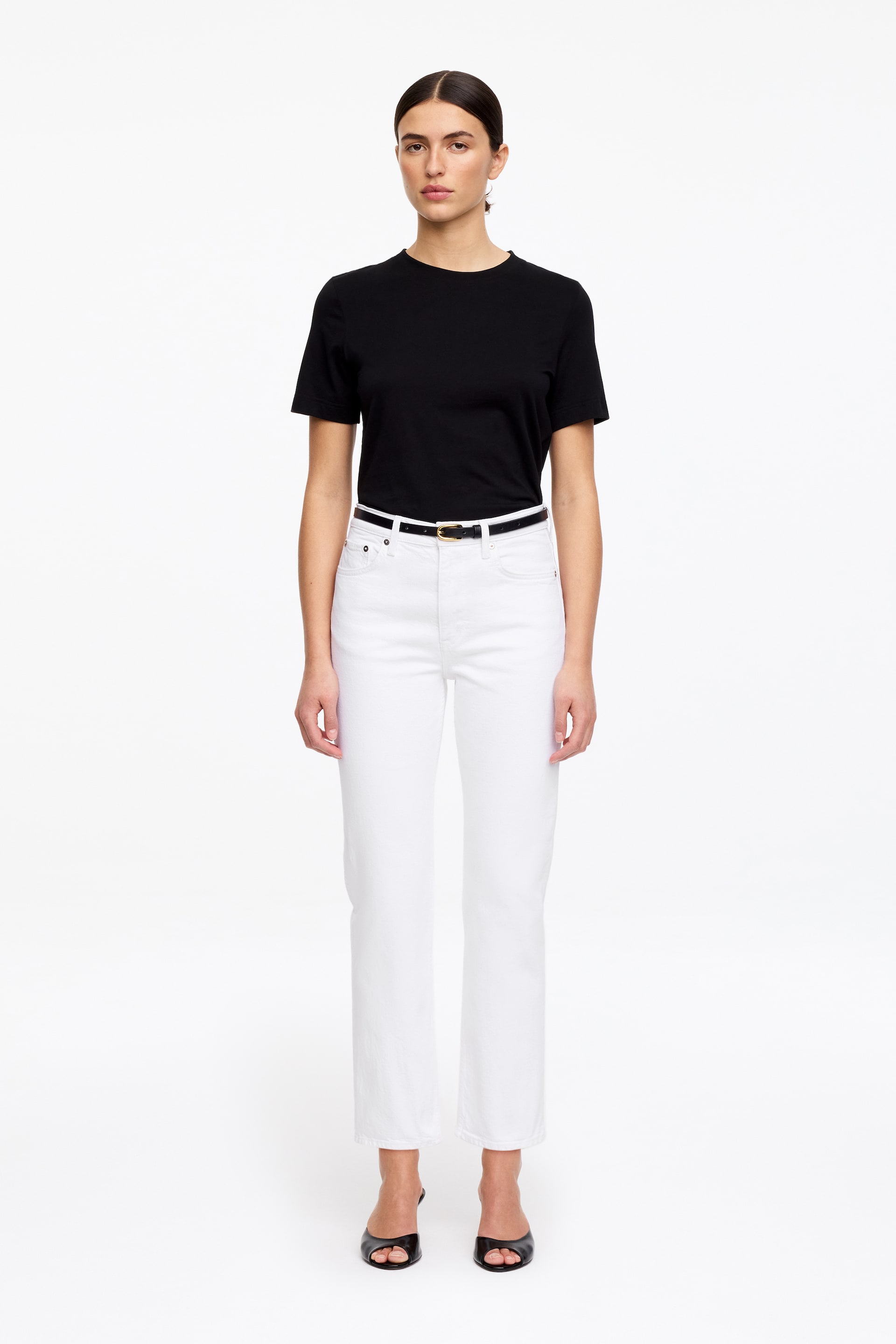 Ver imagen más grande: Se lleva una camiseta negra de cuello redondo, metida dentro de unos vaqueros blancos de pierna recta. Los vaqueros de talle alto cuentan con un fino cinturón negro con hebilla dorada.