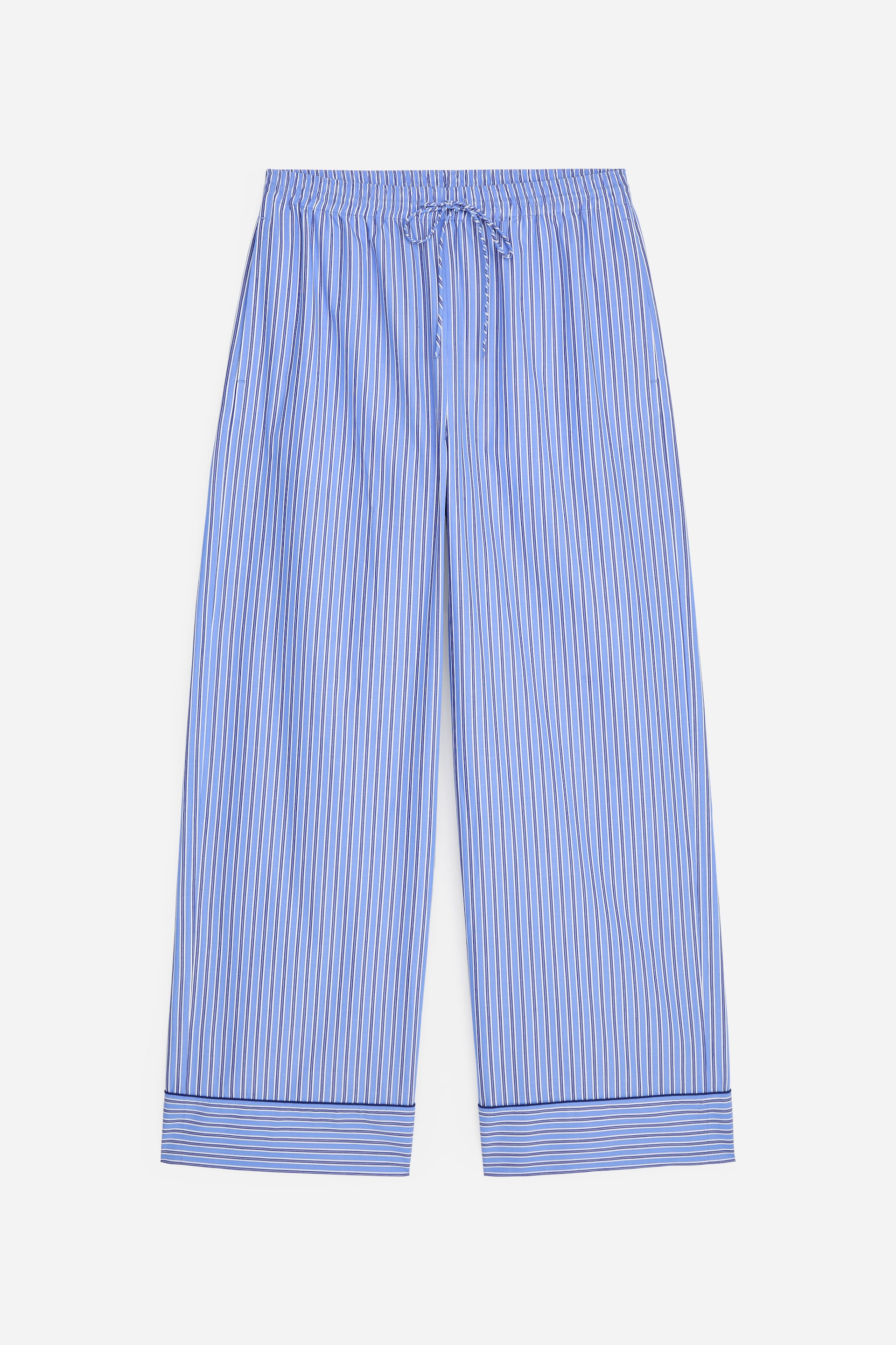 Grotere afbeelding bekijken: Pyjamabroeken tonen een blauw-wit verticaal gestreept patroon met dunne accentlijnen. Ze hebben een elastische tailleband met trekkoord en wijde pijpen met omgeslagen zomen, afgewerkt met een donkerblauwe bies.