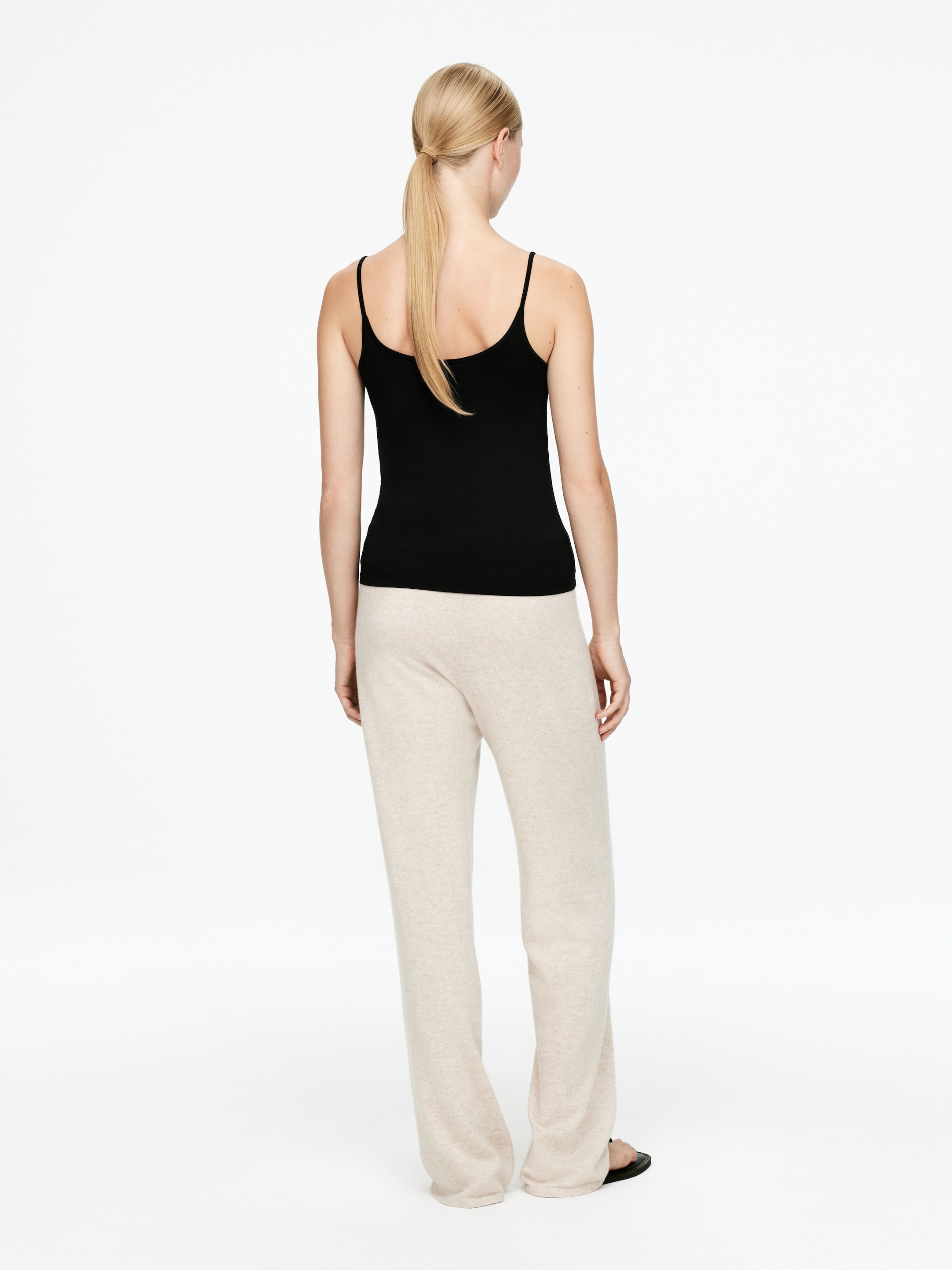 Visualizza immagine più grande: Un top nero a canotta e pantaloni a maglia beige chiaro a gamba larga sono indossati, visti da dietro. La canotta presenta sottili spalline a spaghetti e una silhouette aderente con un retro dritto, mentre i pantaloni mostrano una vestibilità rilassata che si accumula leggermente alle caviglie.