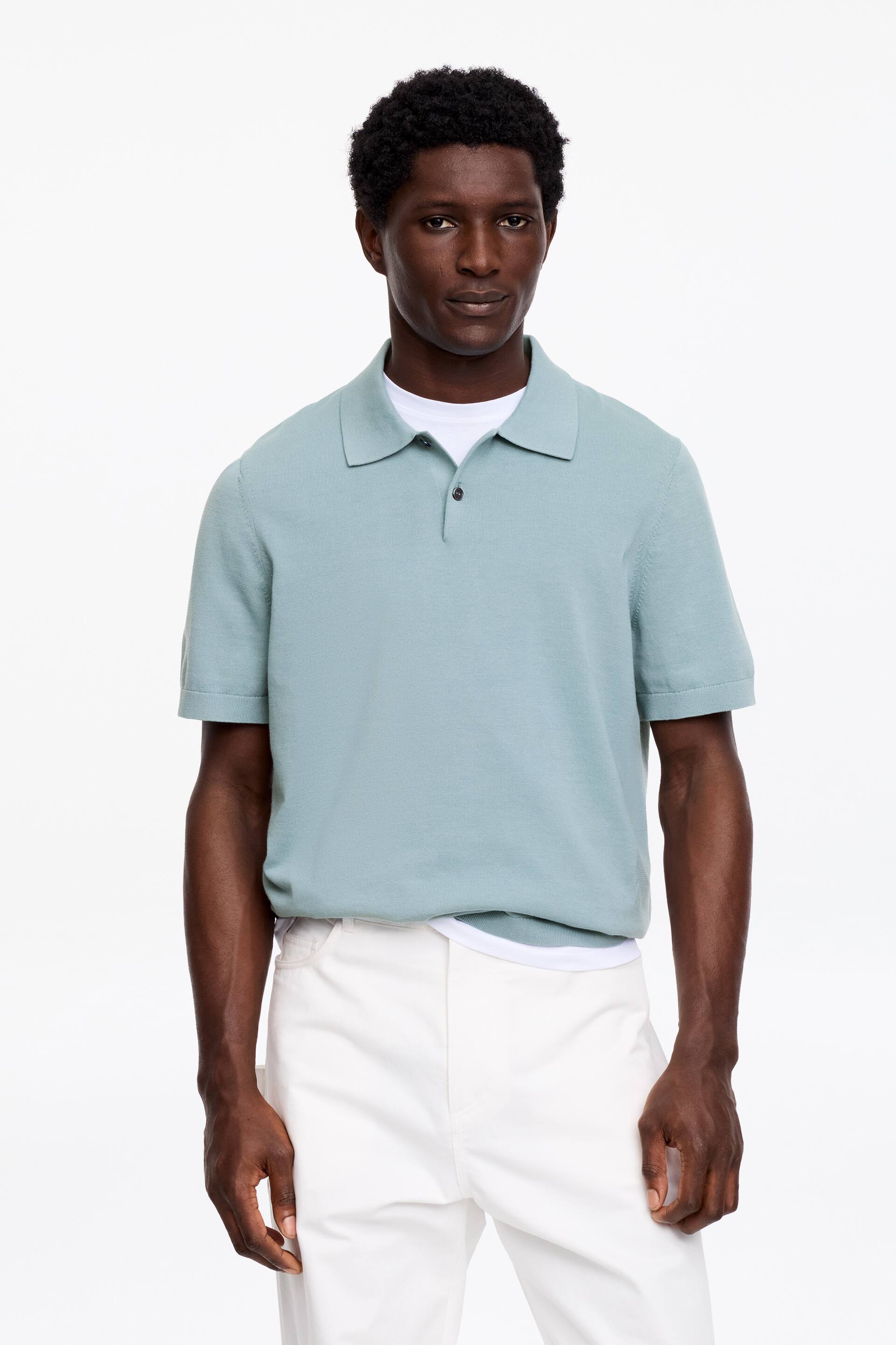 Zobrazit větší obrázek: Světlý tyrkysový pletený polo tričko s krátkými rukávy, které má klasický límec a dvouknoflíkovou légu s tmavými knoflíky. Pod ním je viditelně vrstvené bílé tričko.
