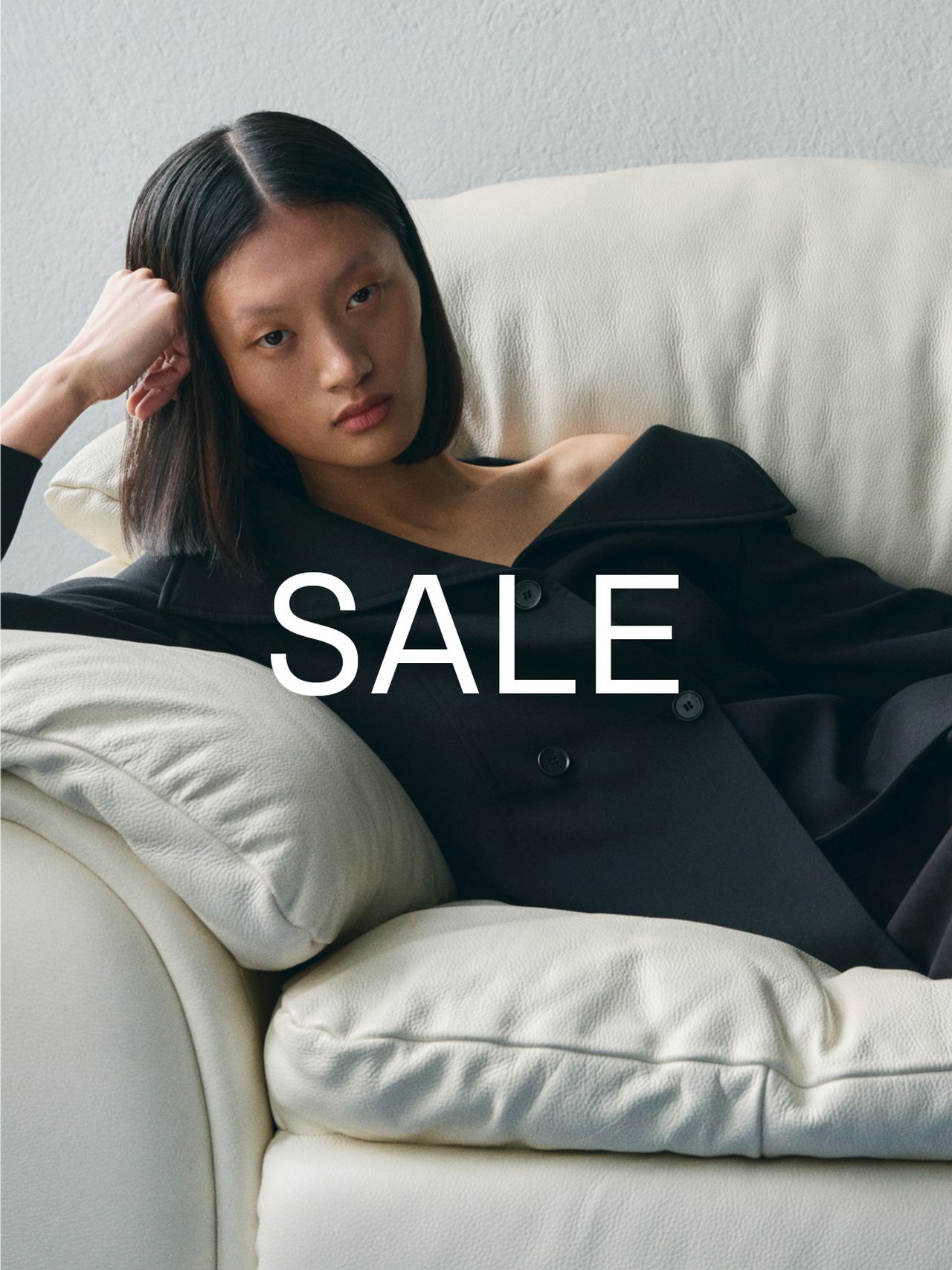 Person in a black coat reclines on a white sofa, with "SALE" text overlayed on the image.