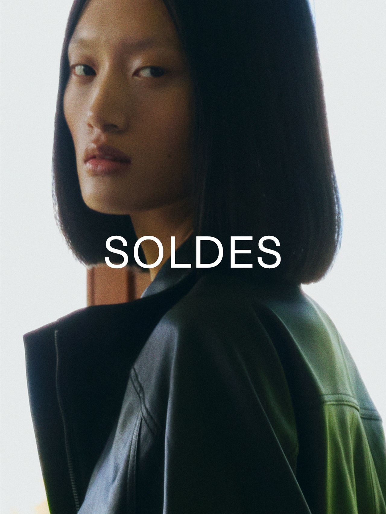 Person with shoulder-length hair in a leather jacket, looking over their shoulder. The word "SOLDES" is overlaid on the image.