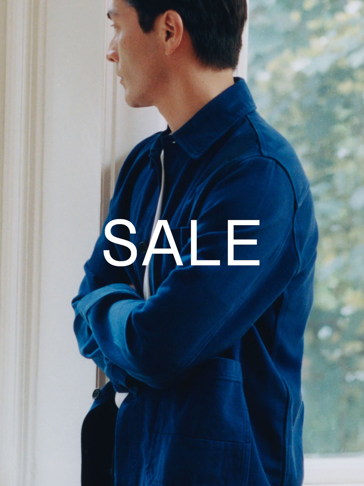 Man in a blue jacket stands by a window, arms crossed, with "SALE" in bold white text overlaying the image.