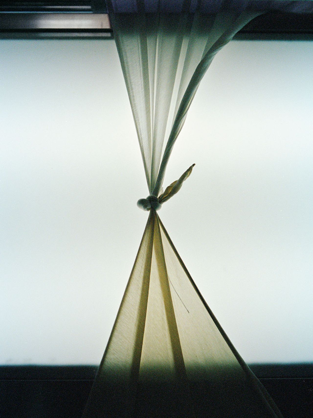 Sheer curtain tied in a knot against a frosted window, creating a soft, diffused light effect.