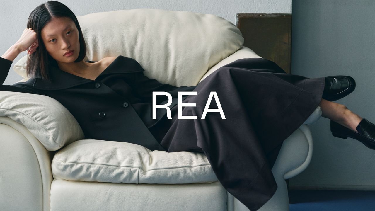Person in a black outfit lounging on a white sofa, with the word "REA" overlaid on the image.