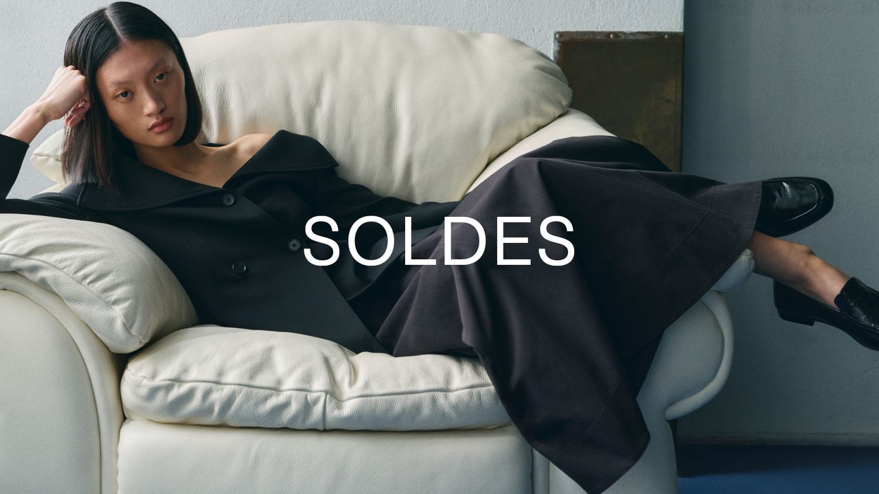 Woman in a black outfit reclines on a white sofa, with the word "SOLDES" overlaid in white text.