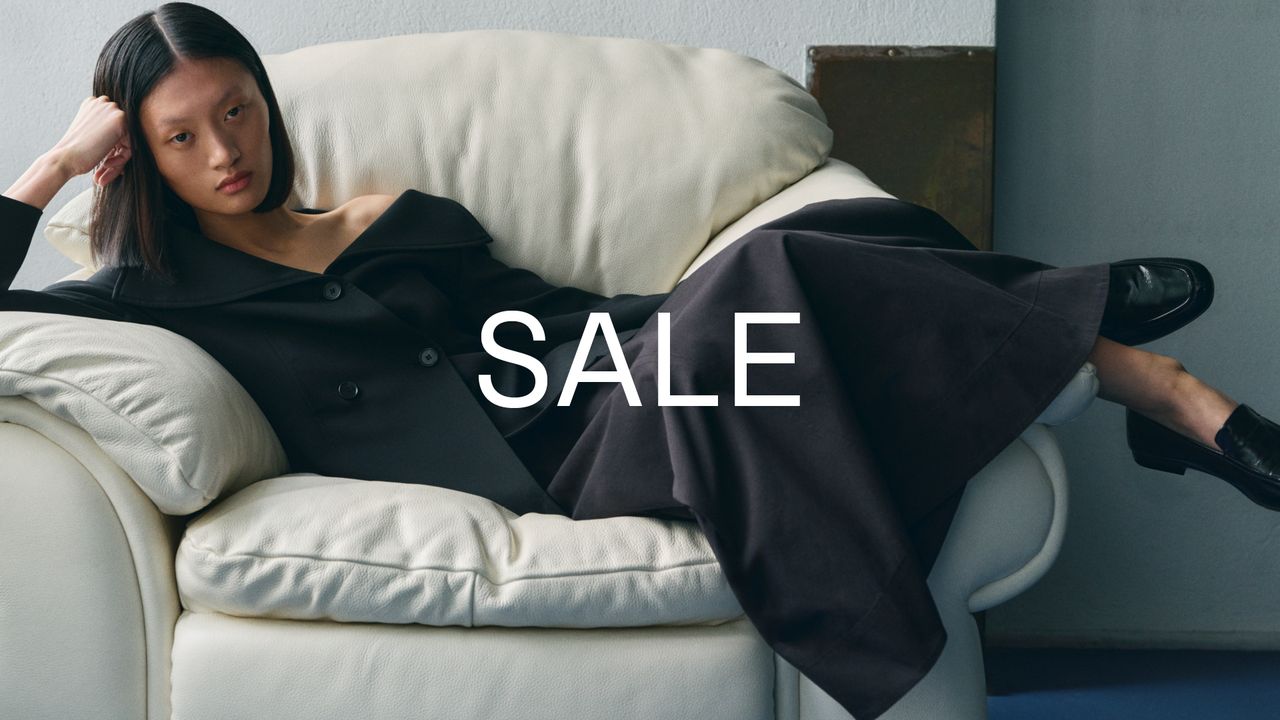 Person lounging on a white couch wearing dark clothing, with the word "SALE" overlaid in large white letters.