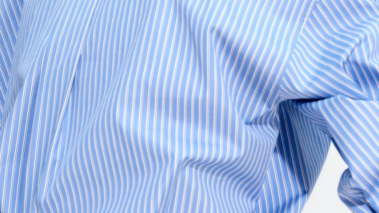 Close-up of a blue and white vertically striped shirt with a smooth, wrinkle-free fabric texture, showing partial view of the sleeve and torso.