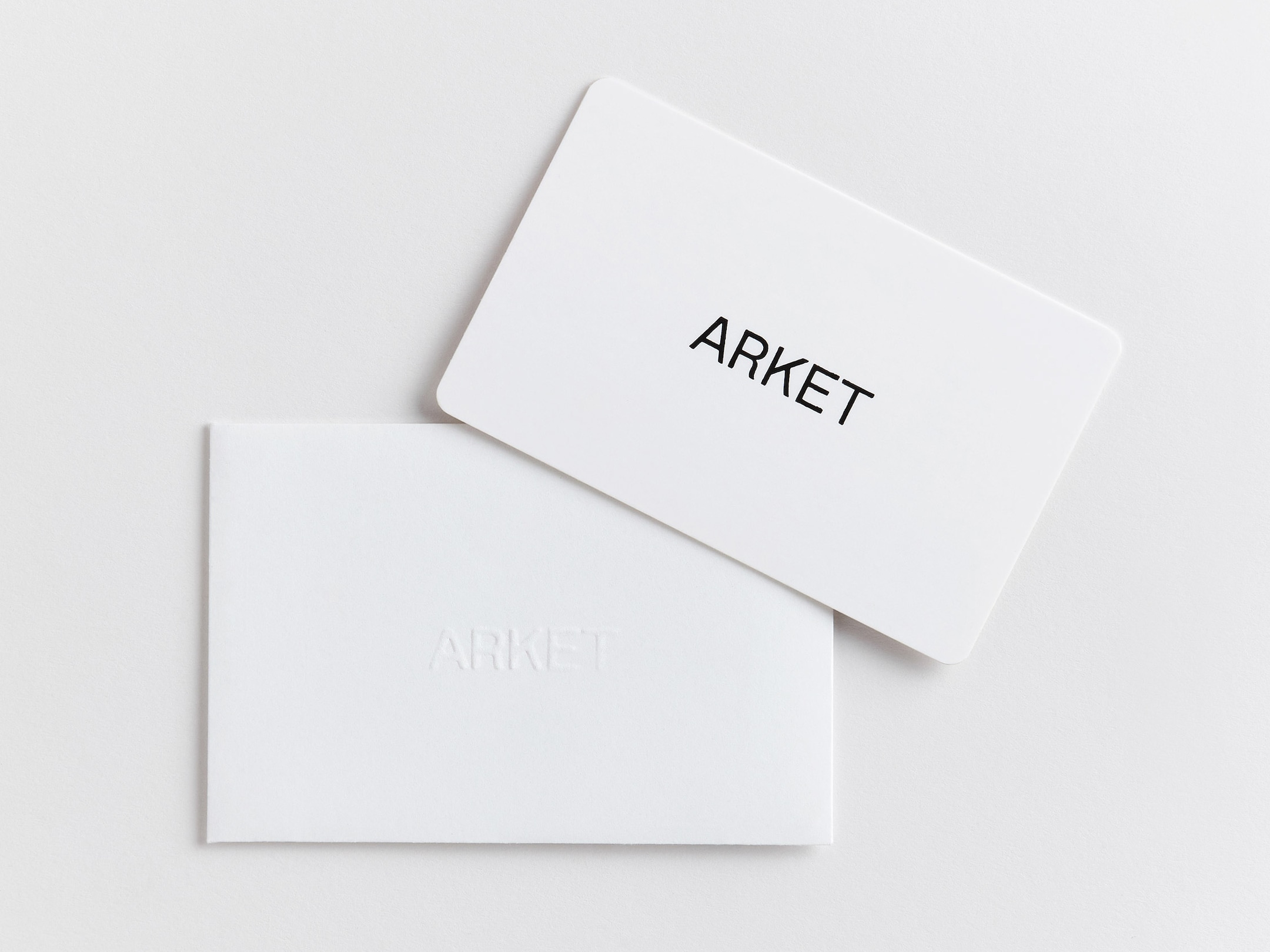 White gift card with "ARKET" in black text, placed on a white embossed envelope with the same text. Minimalist design on a plain background.