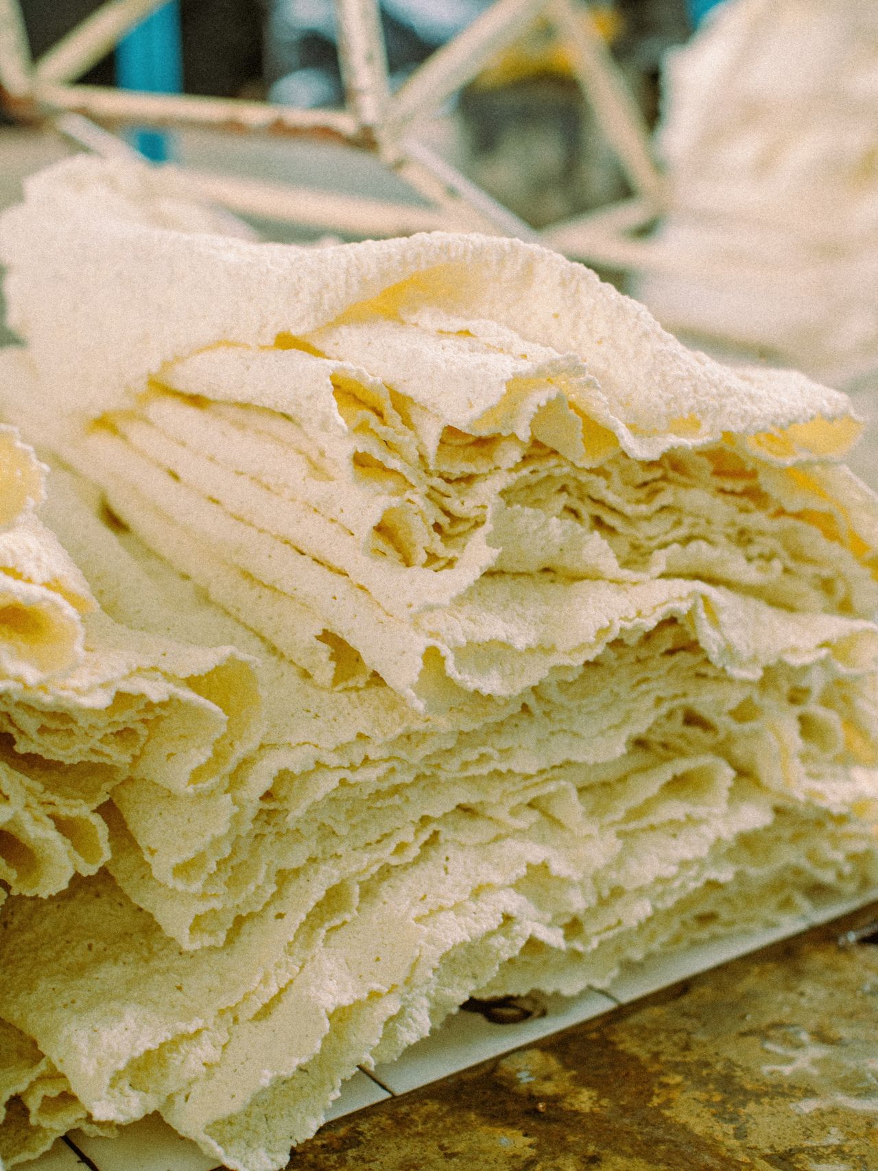 A stack of thin, irregularly shaped, light-colored sheets arranged in layers on a rustic surface, with a blurred background.