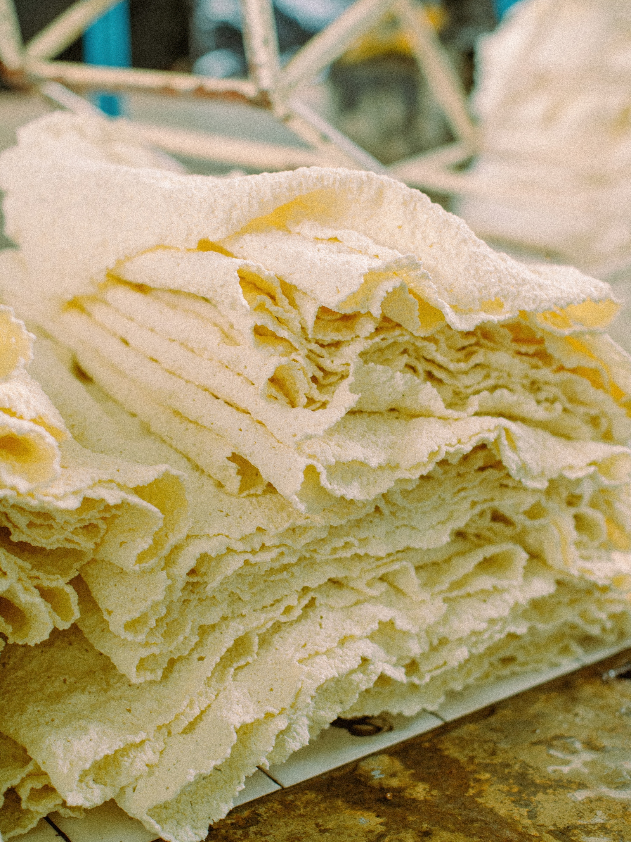 A stack of thin, irregularly shaped, light-colored sheets arranged in layers on a rustic surface, with a blurred background.