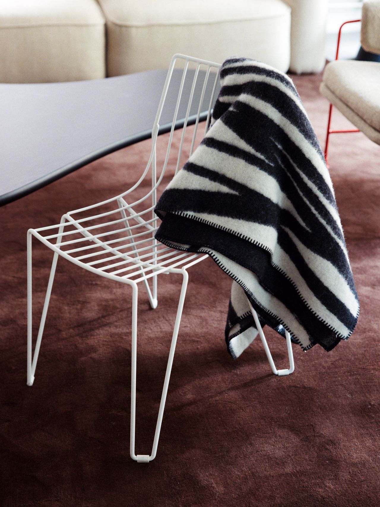 A white wire chair with a black and white zebra-patterned blanket draped over it, on a brown carpeted floor.
