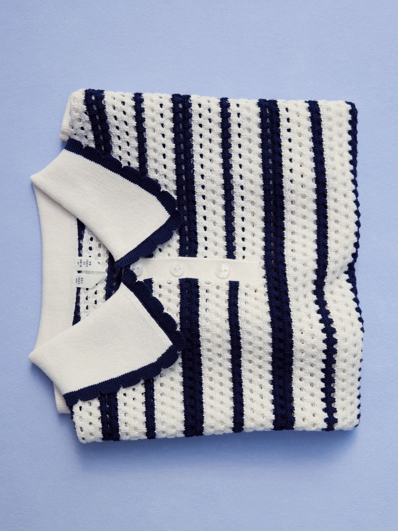 Folded white crochet polo shirt with navy stripes and collar, placed on a light blue background.