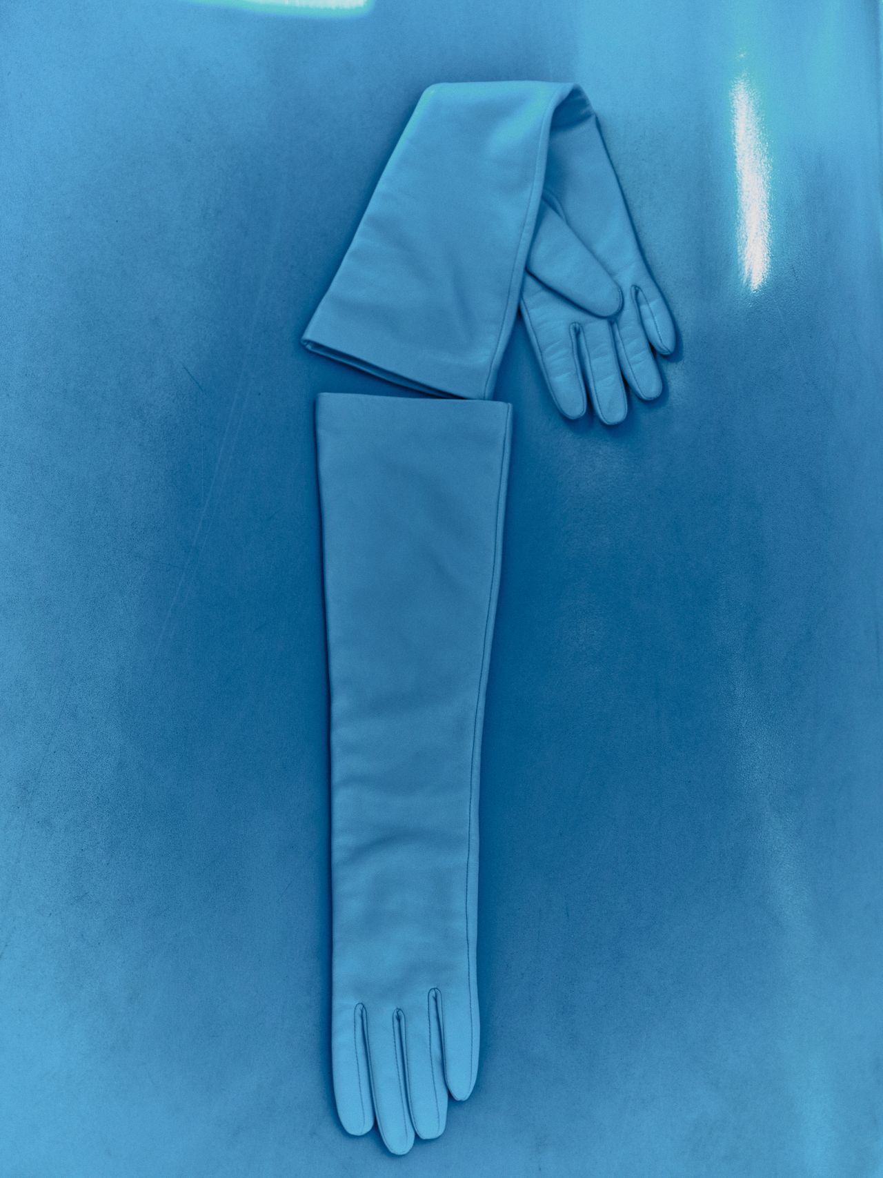 Long blue leather gloves with extended cuffs, laid flat on a reflective blue surface.