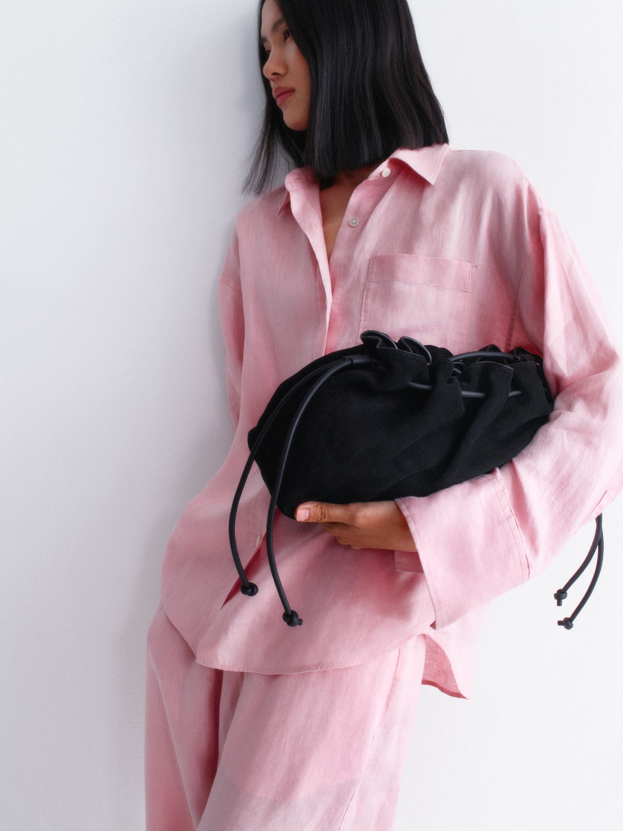 Woman in a pink outfit holds a black drawstring bag, looking to the side against a plain white background.