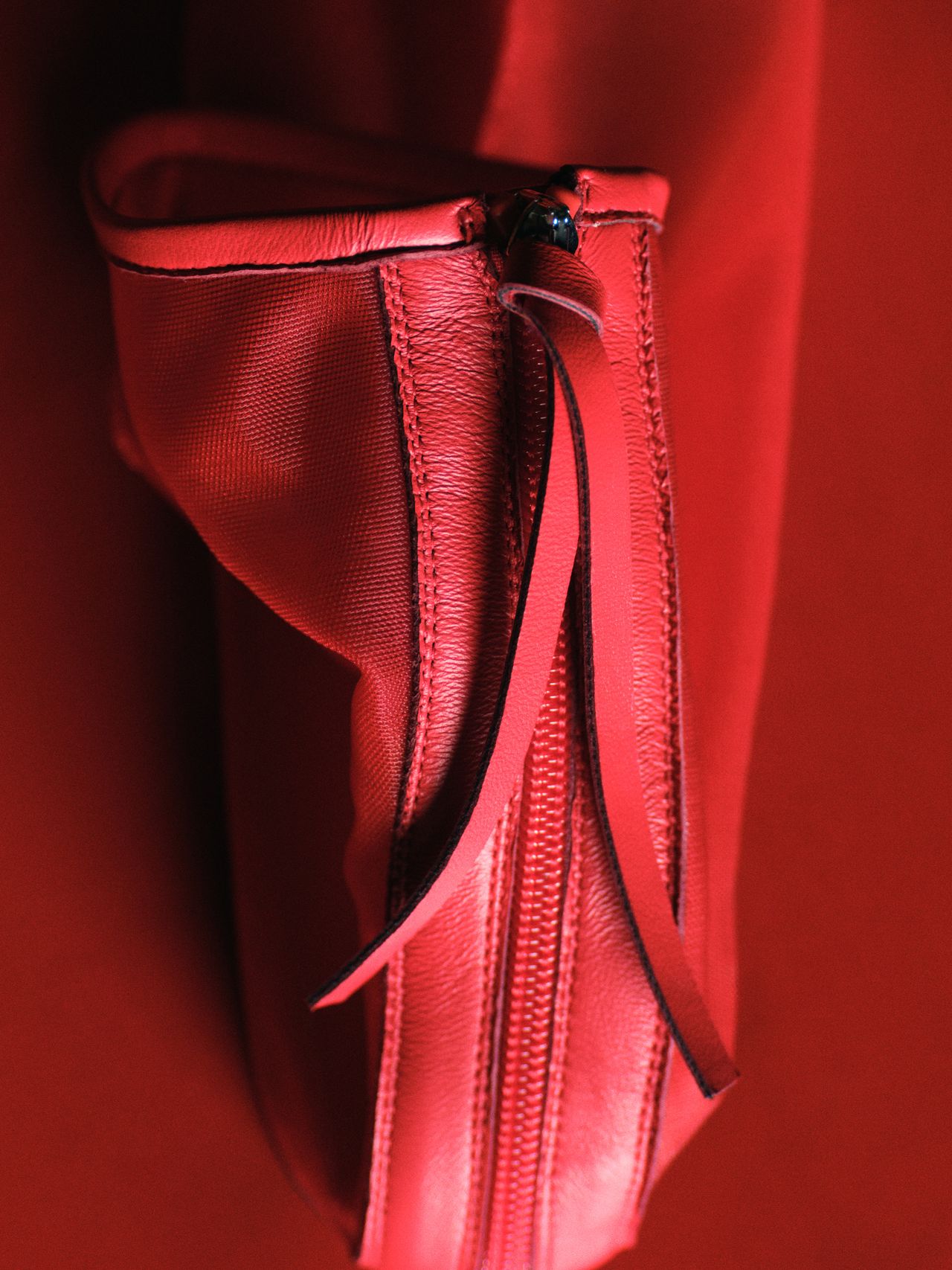 Close-up of a red leather bag with a zipper and a thin strap, set against a matching red background.