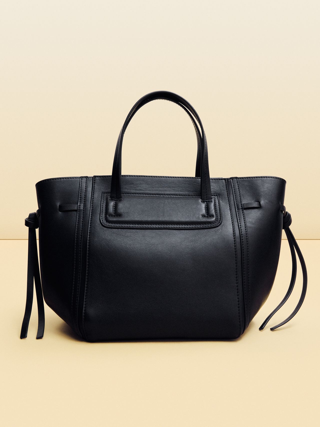 Sleek black leather handbag with dual handles and side tassels, set against a neutral background.