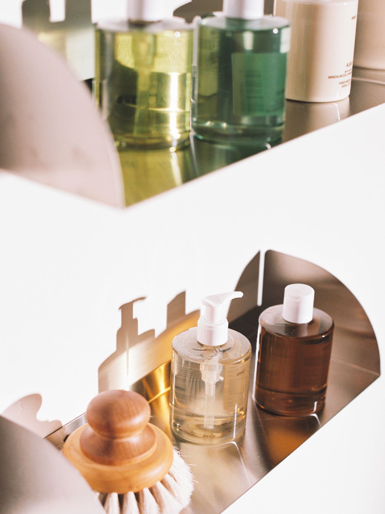 Shelves with various skincare bottles, a wood-handled brush, and pump containers in a softly lit, organized setting.