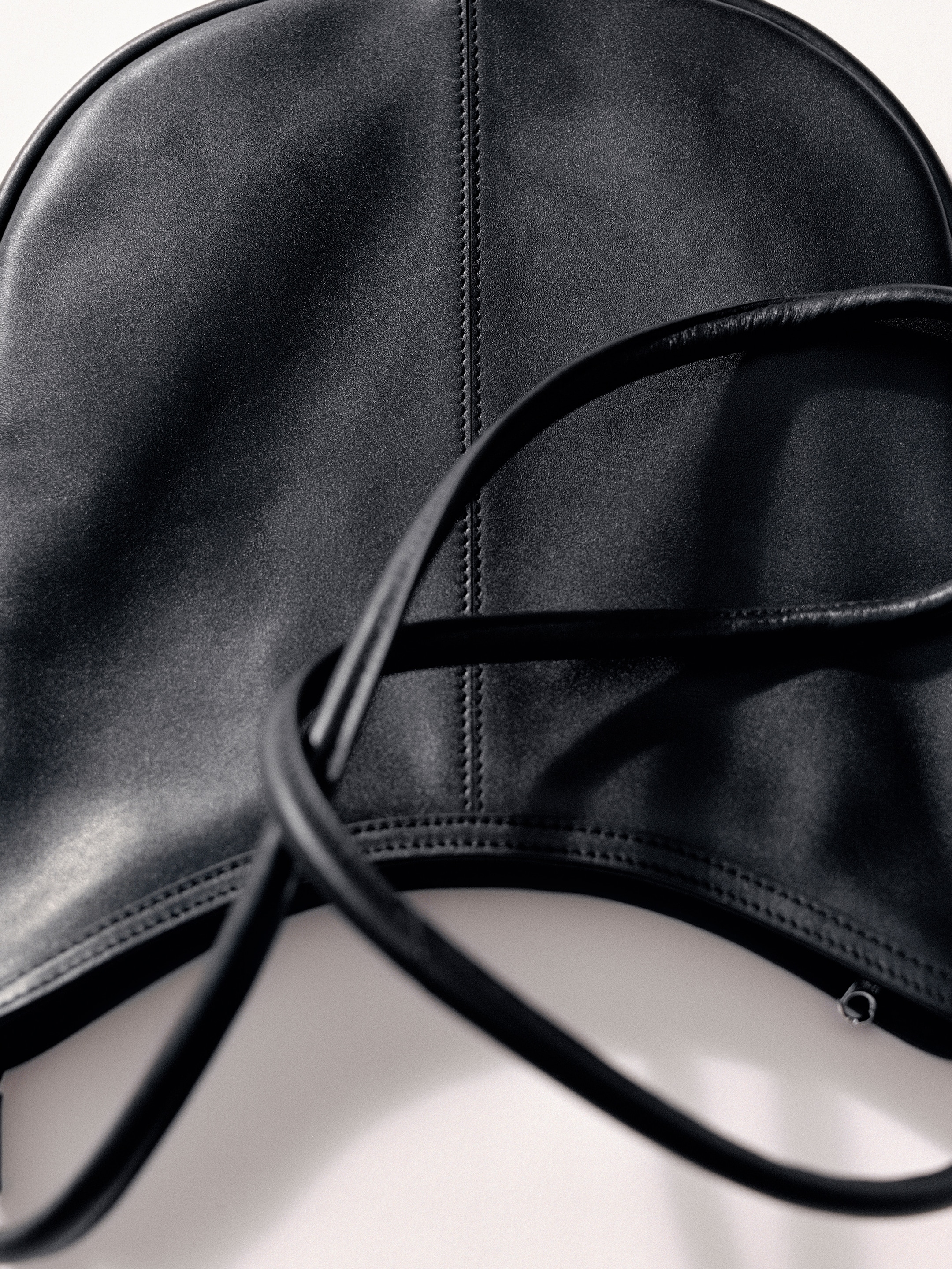 Close-up of a black leather bag with a curved top and two intertwined straps, highlighting the texture and stitching details.