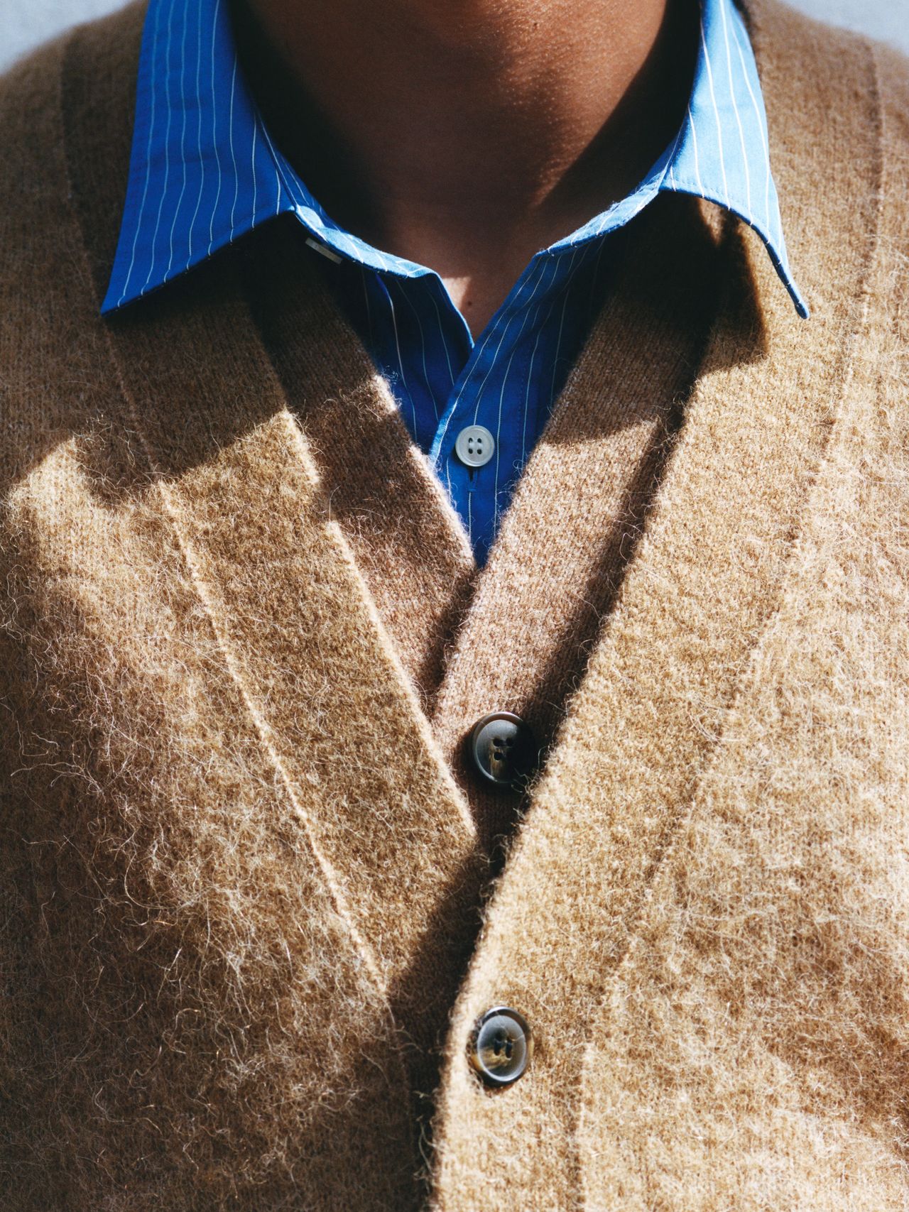 Close-up of a person wearing a brown fuzzy cardigan over a blue striped shirt. The focus is on the textures and buttons of the cardigan.