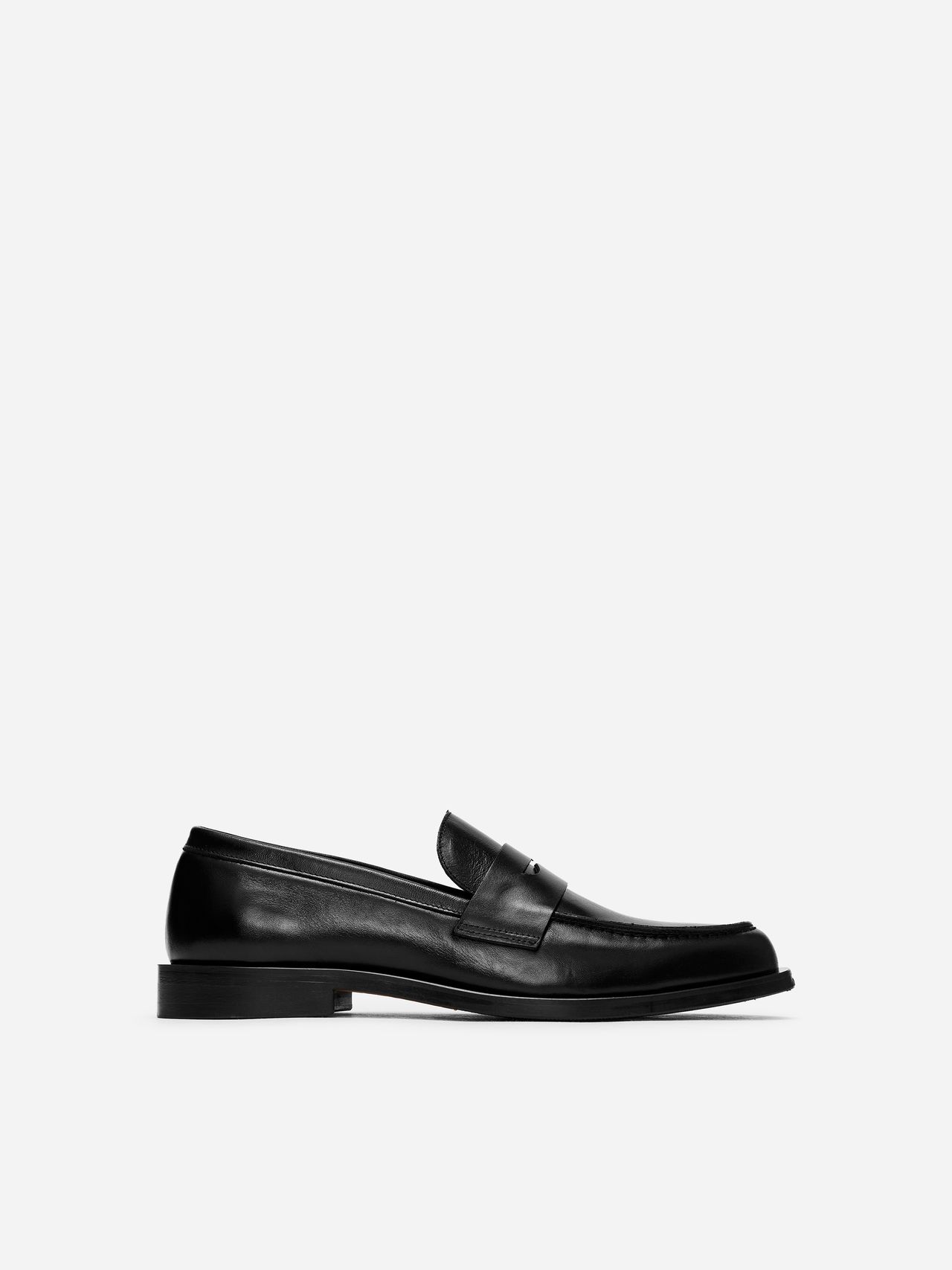 Black leather loafer shoe with a minimalist design, featuring a low heel and sleek finish, displayed on a white background.