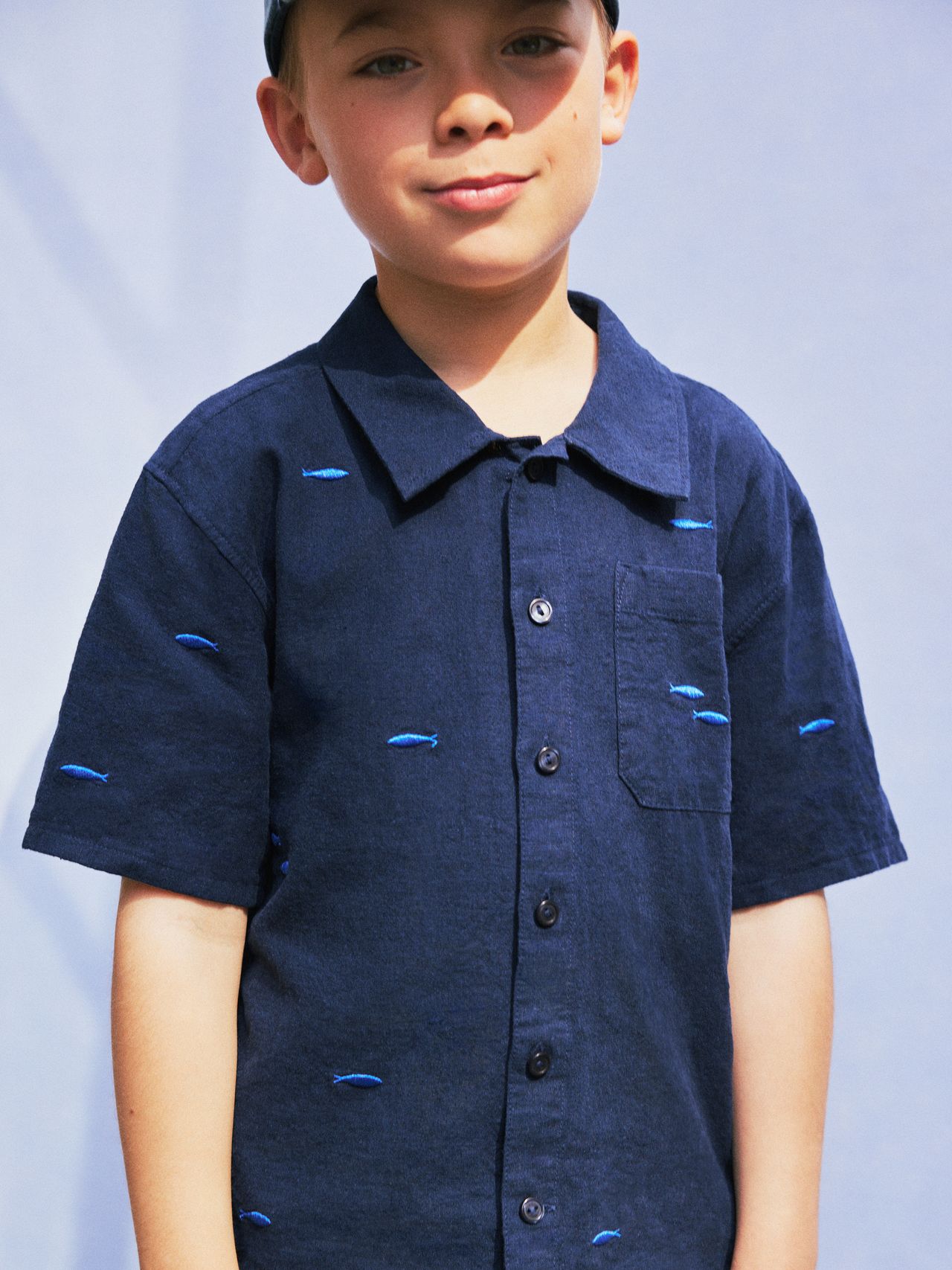 Young boy in a navy shirt with small blue fish patterns, standing against a light blue background.