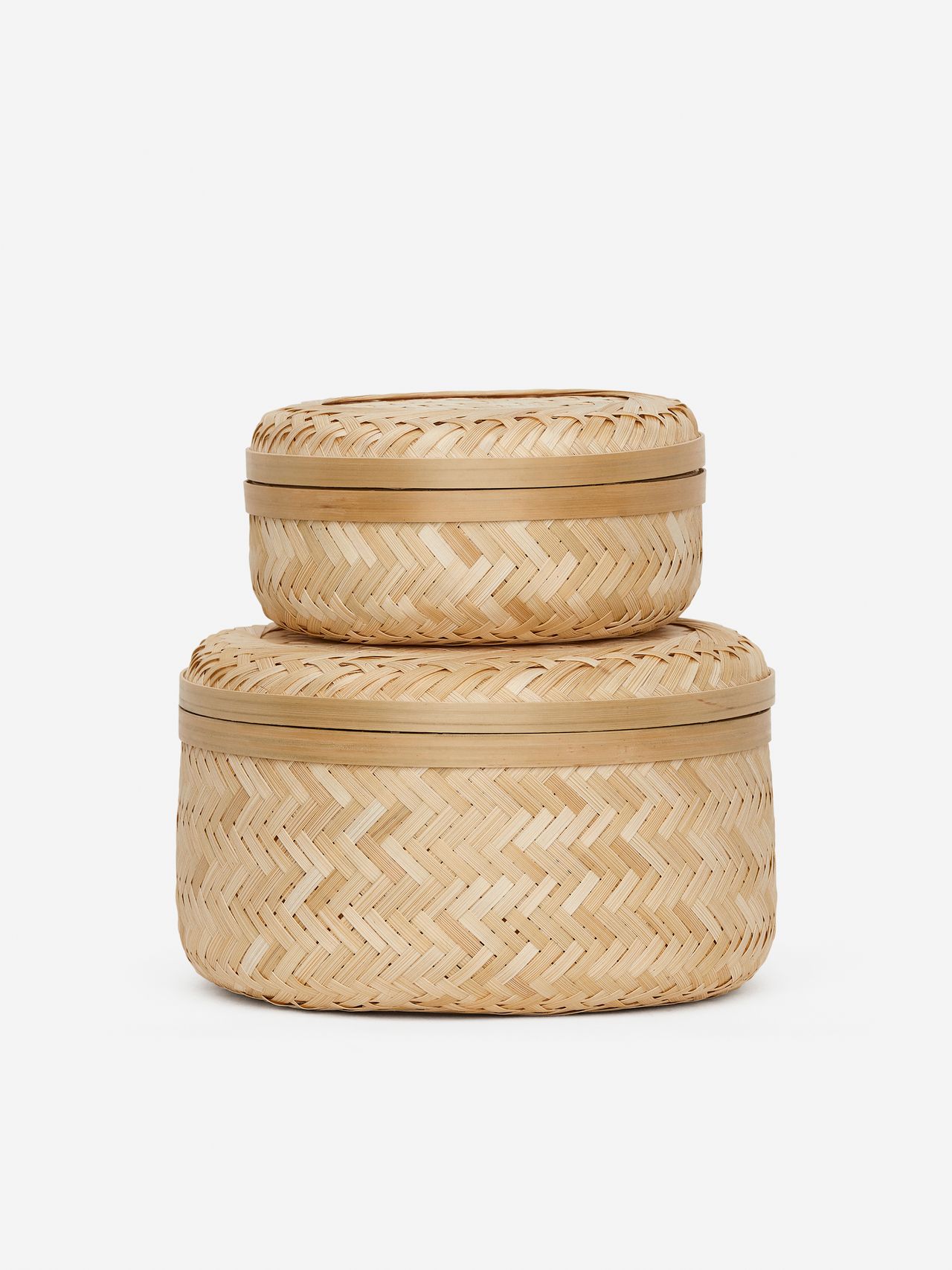 Two nested, round woven baskets with lids, featuring a light natural color and herringbone pattern, set against a plain white background.