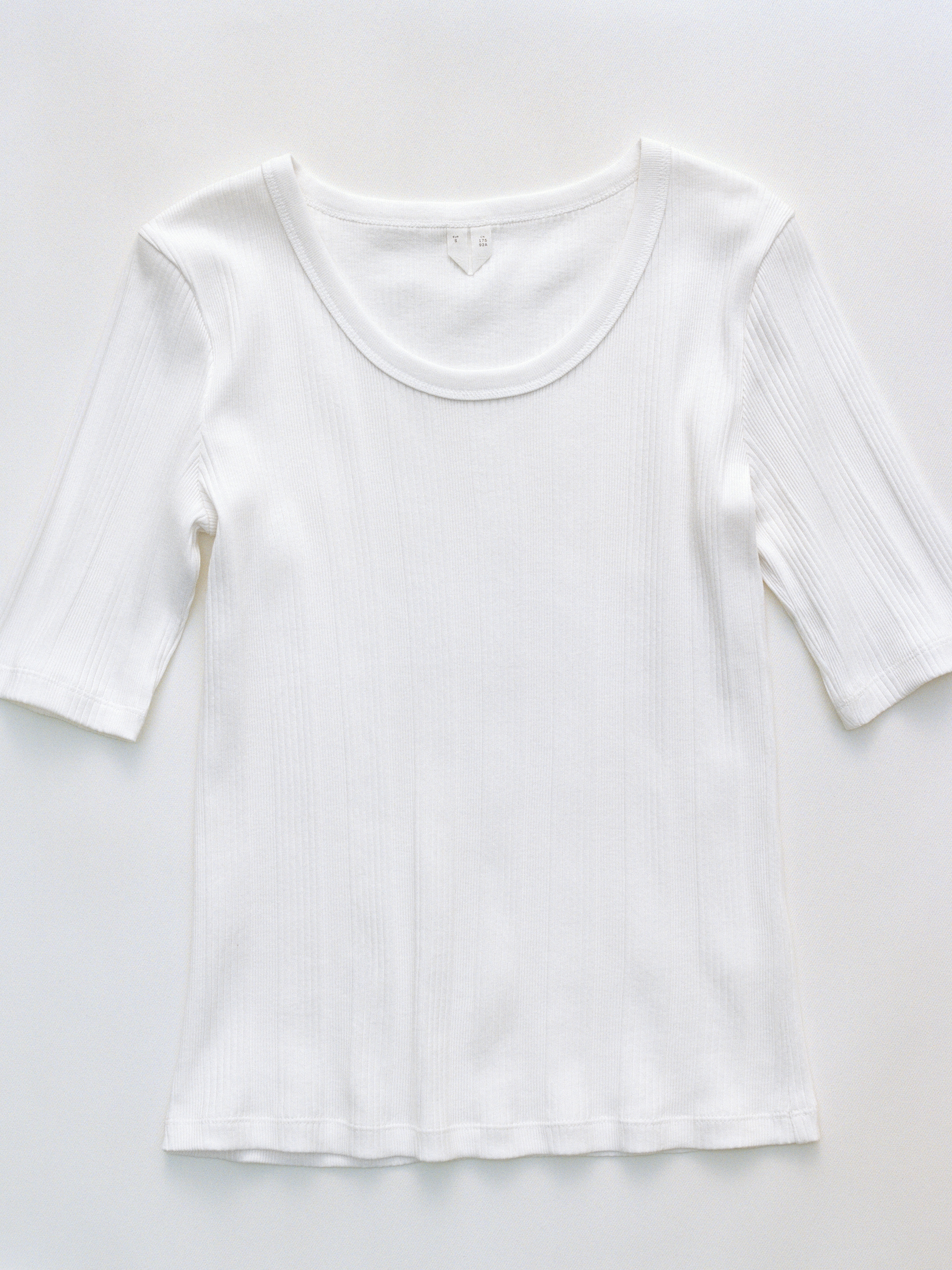 White ribbed short-sleeve shirt with a round neckline, laid flat on a plain surface.