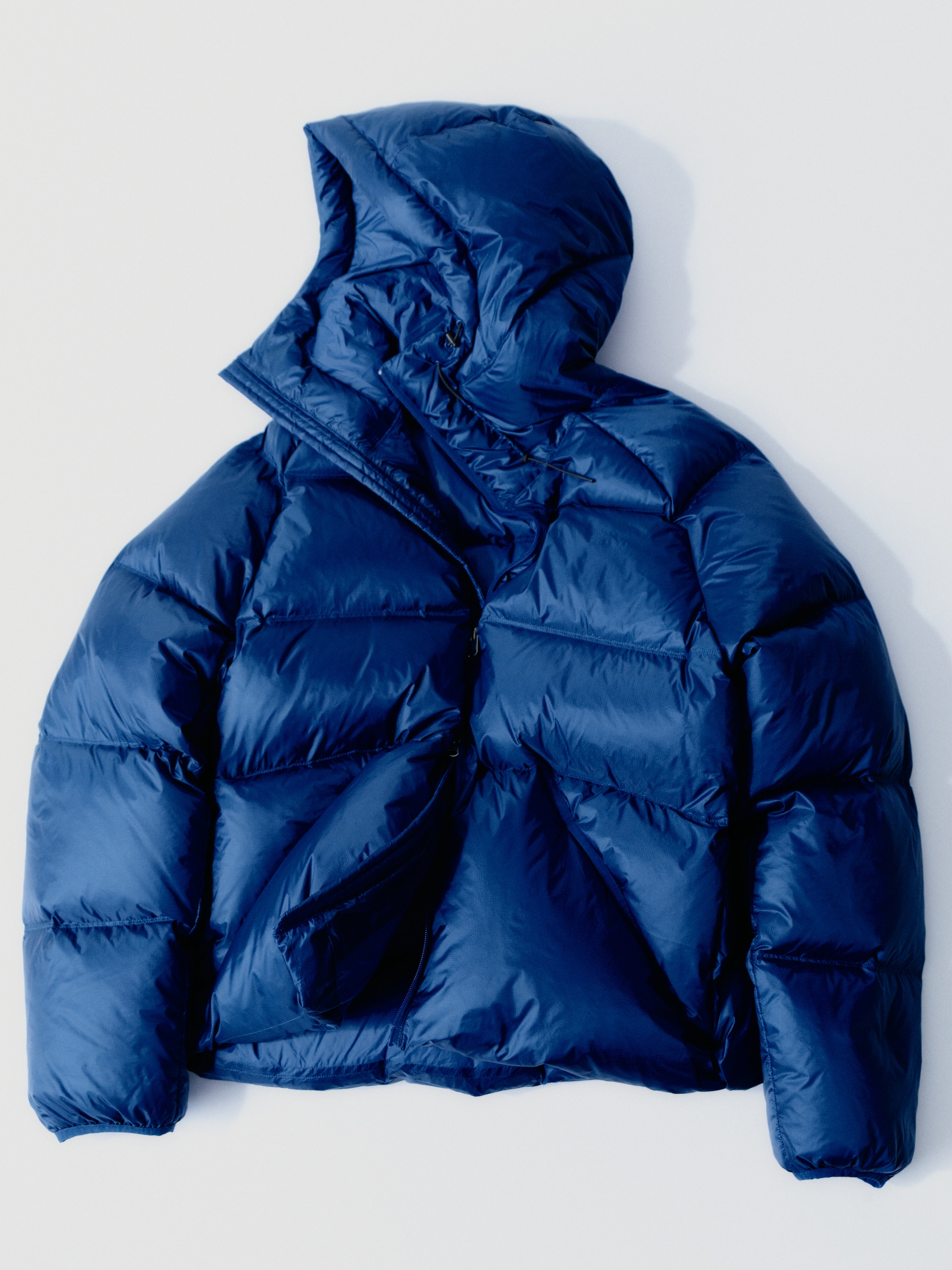 A blue puffer jacket with a hood, laid out on a white background.