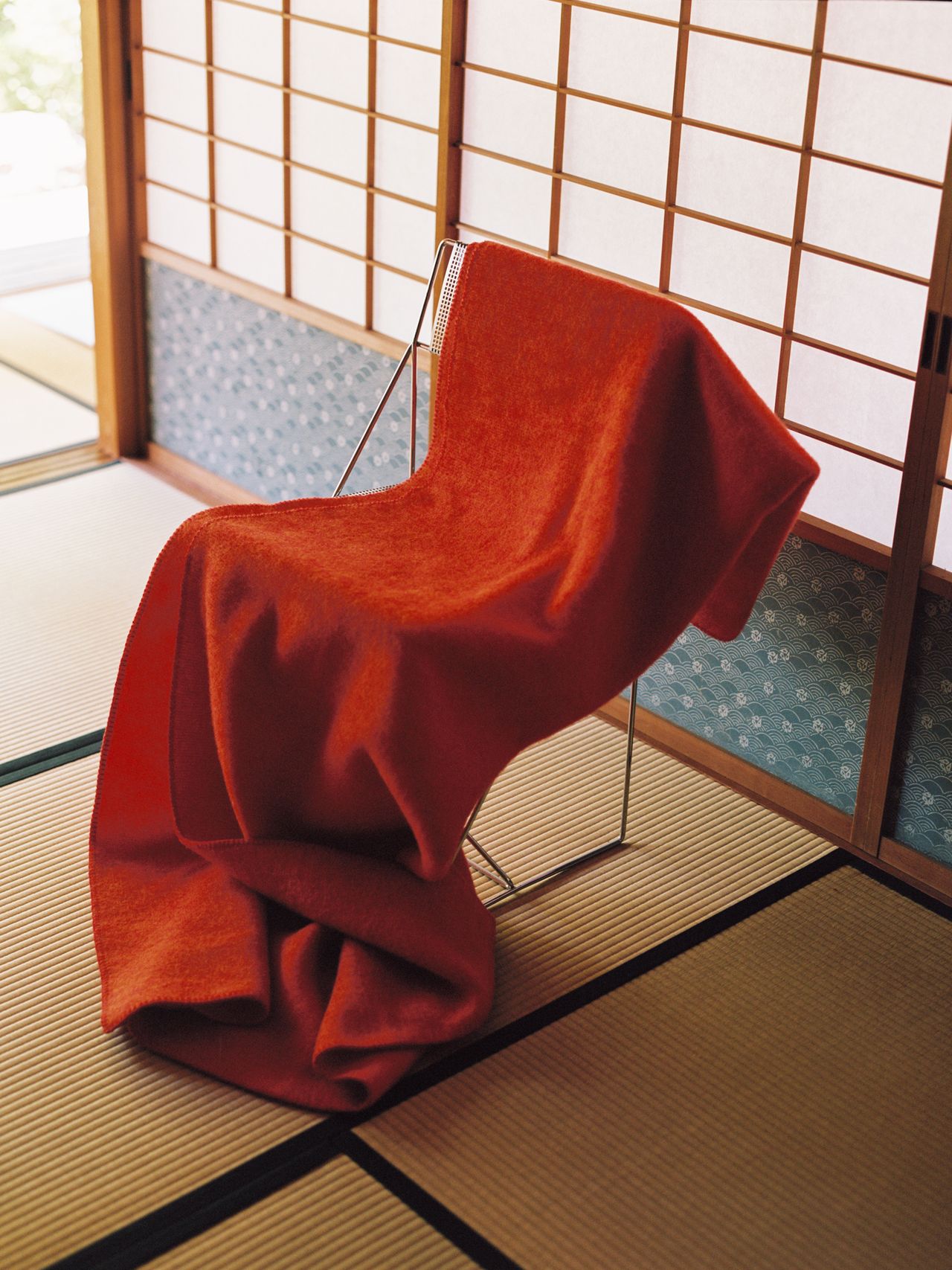 A modern chair draped with a red fabric in a room with shoji screens and tatami mats, creating a serene, minimalist atmosphere.