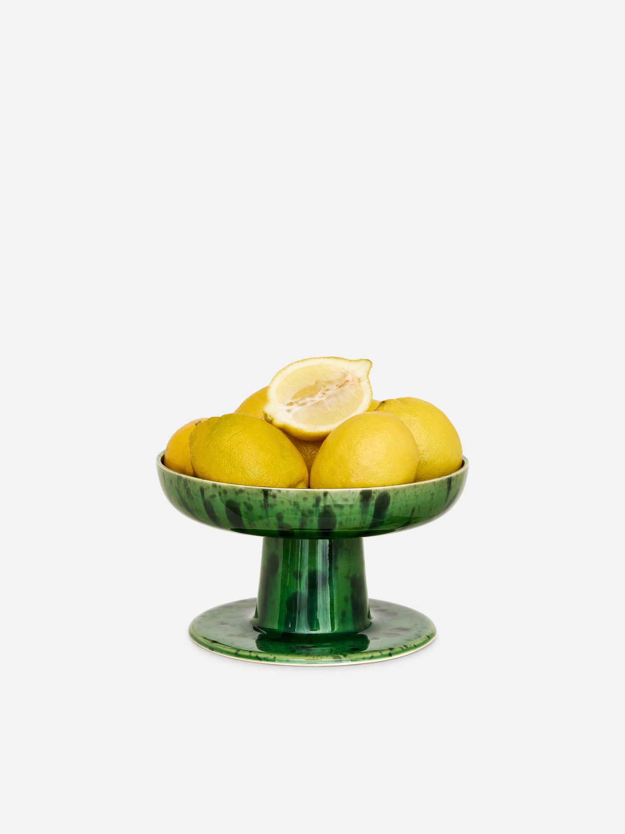Green pedestal bowl with whole lemons and a halved lemon on top, set against a plain white background.