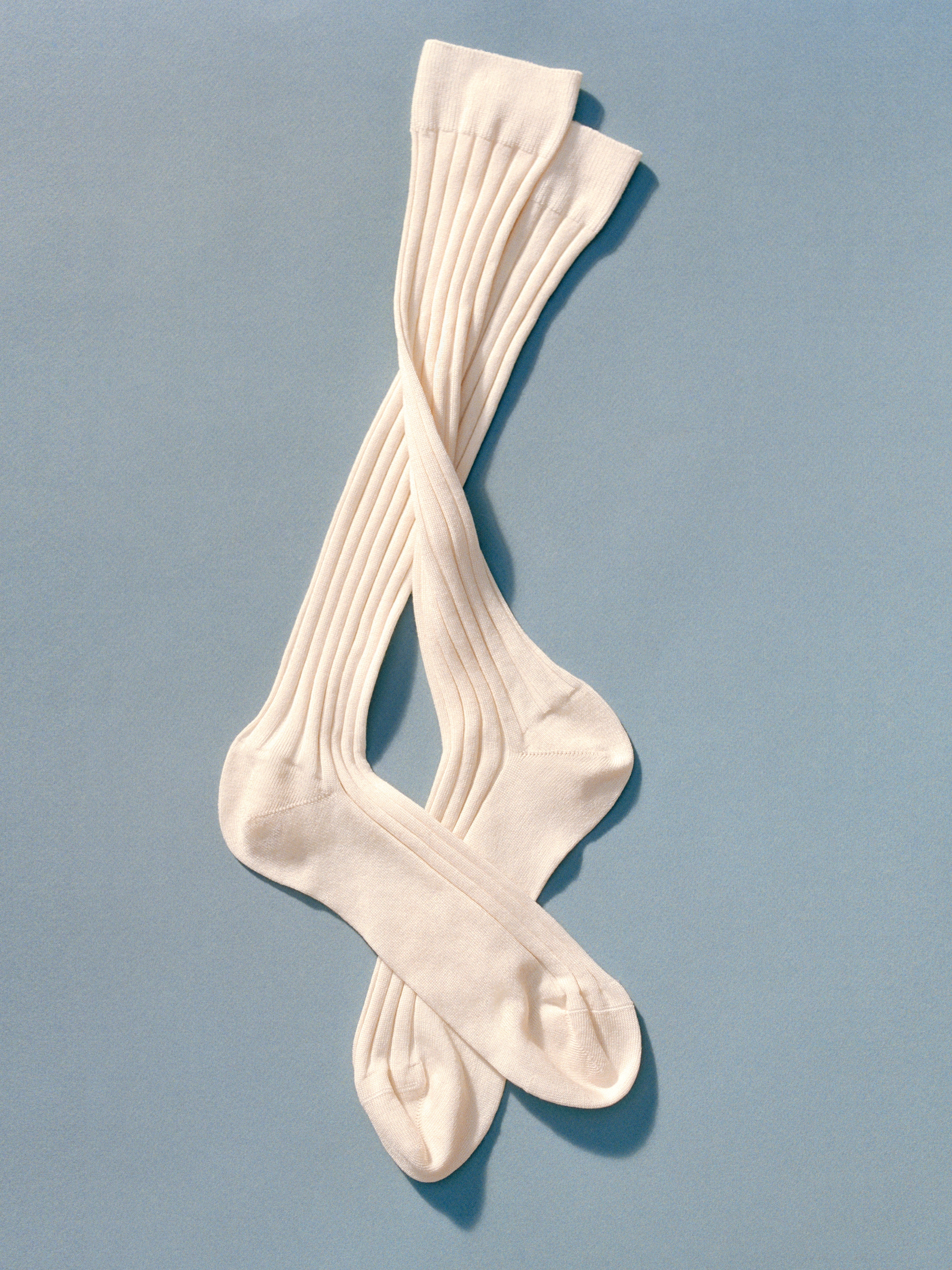 A pair of ribbed, cream-colored knee-high socks laid out on a light blue background, with one sock overlapping the other.