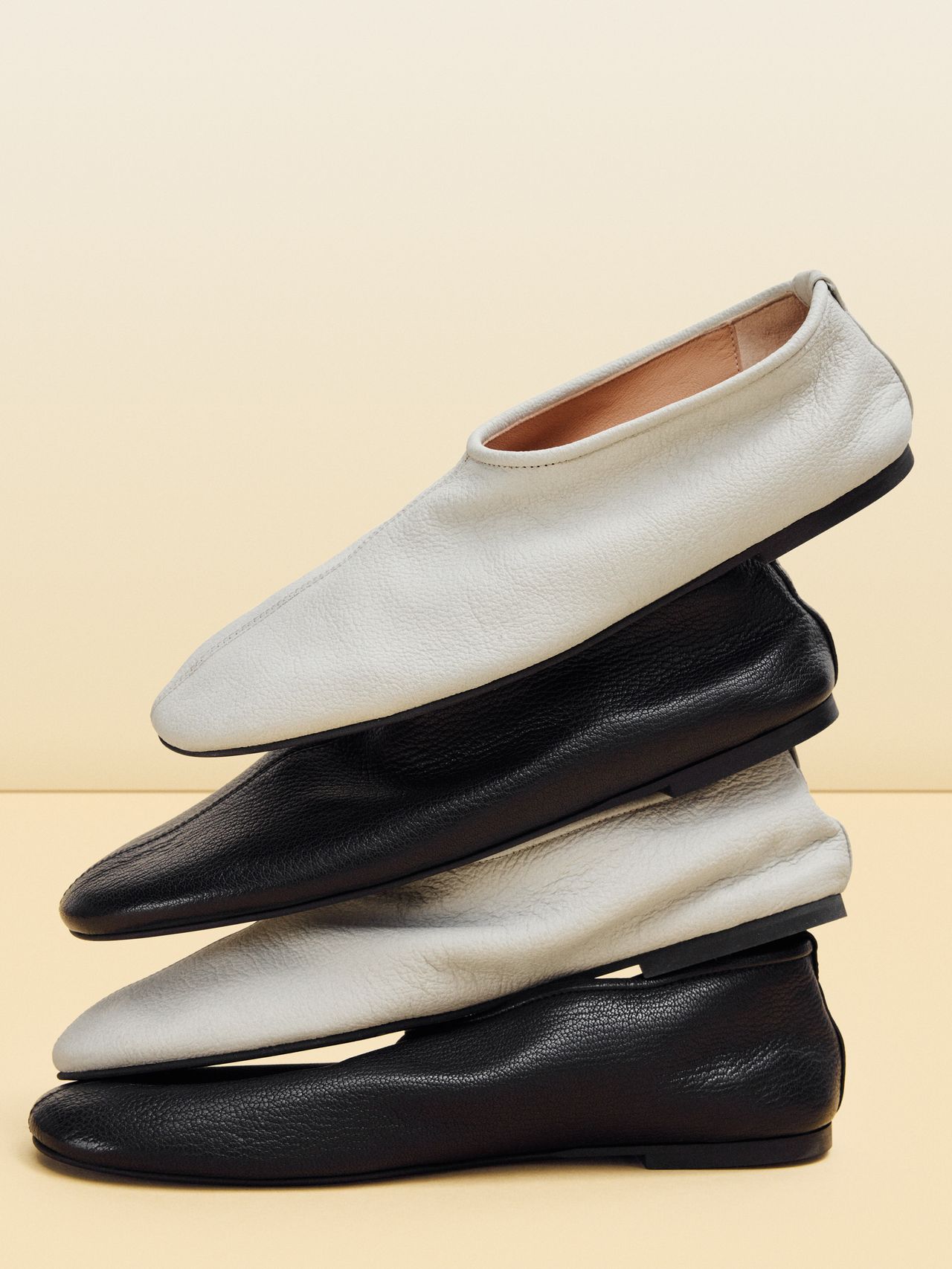 A stack of four minimalist shoes, alternating between white and black, displayed against a neutral background.